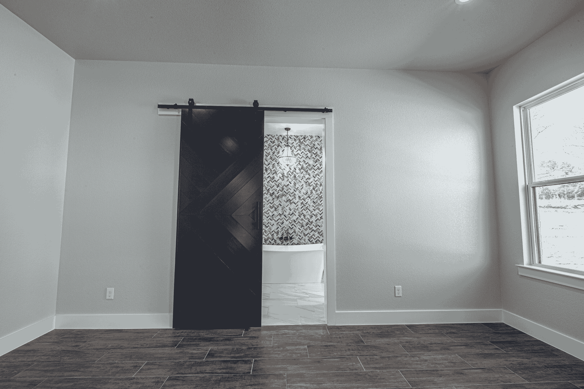 An empty room with a sliding barn door leading to a bathroom.