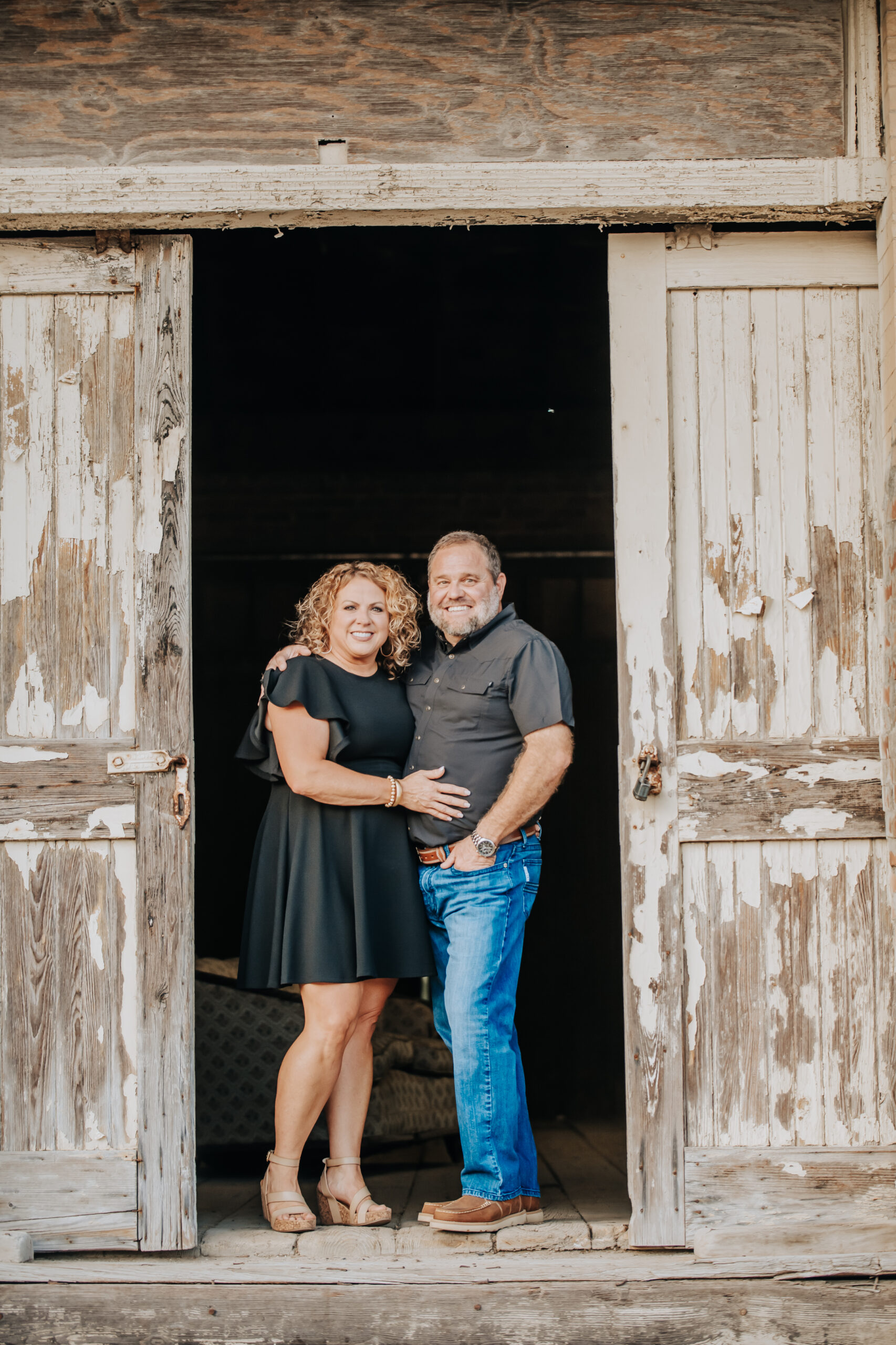A man and a woman are standing in front of a barn door.