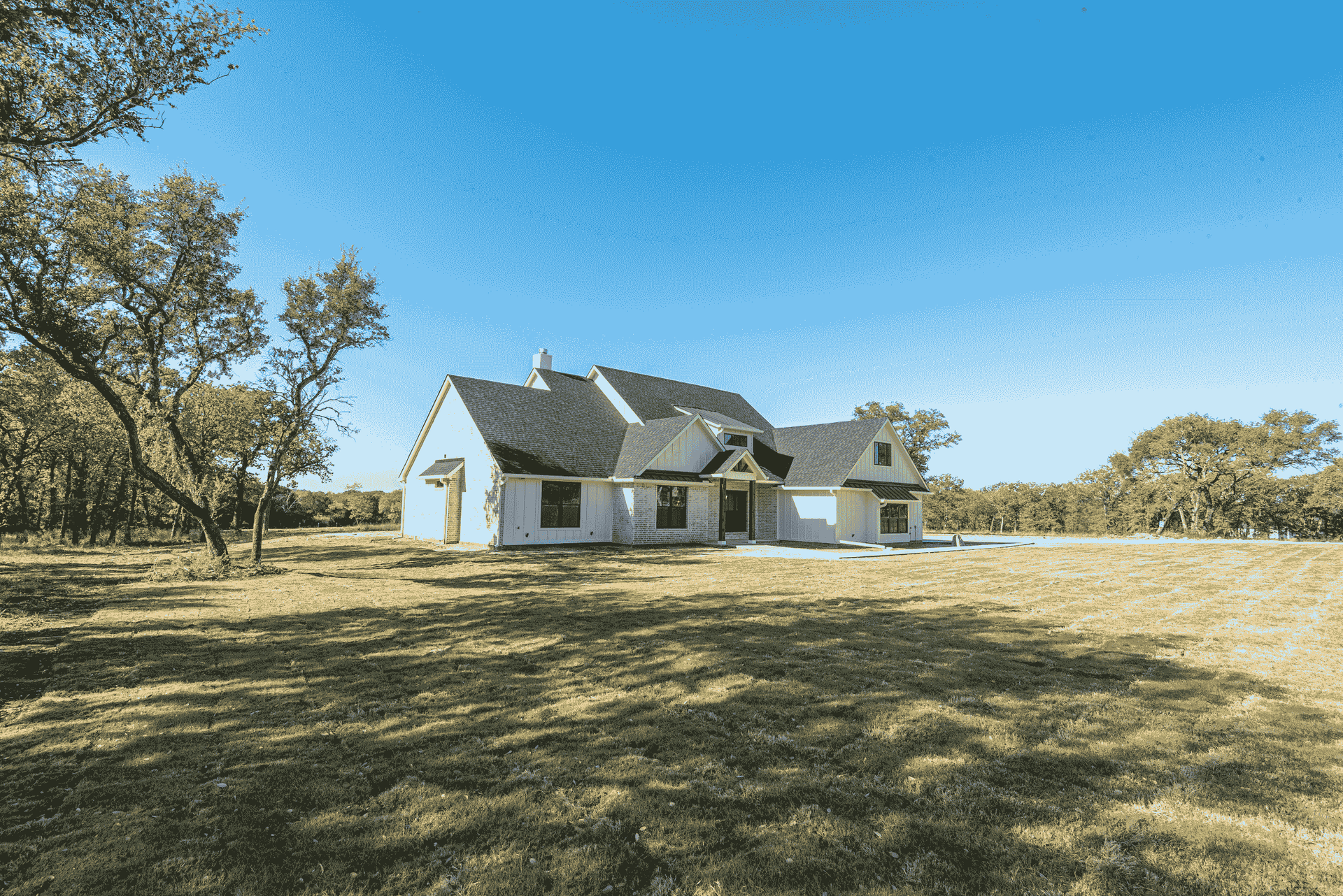 A white house with a black roof is sitting in the middle of a grassy field.
