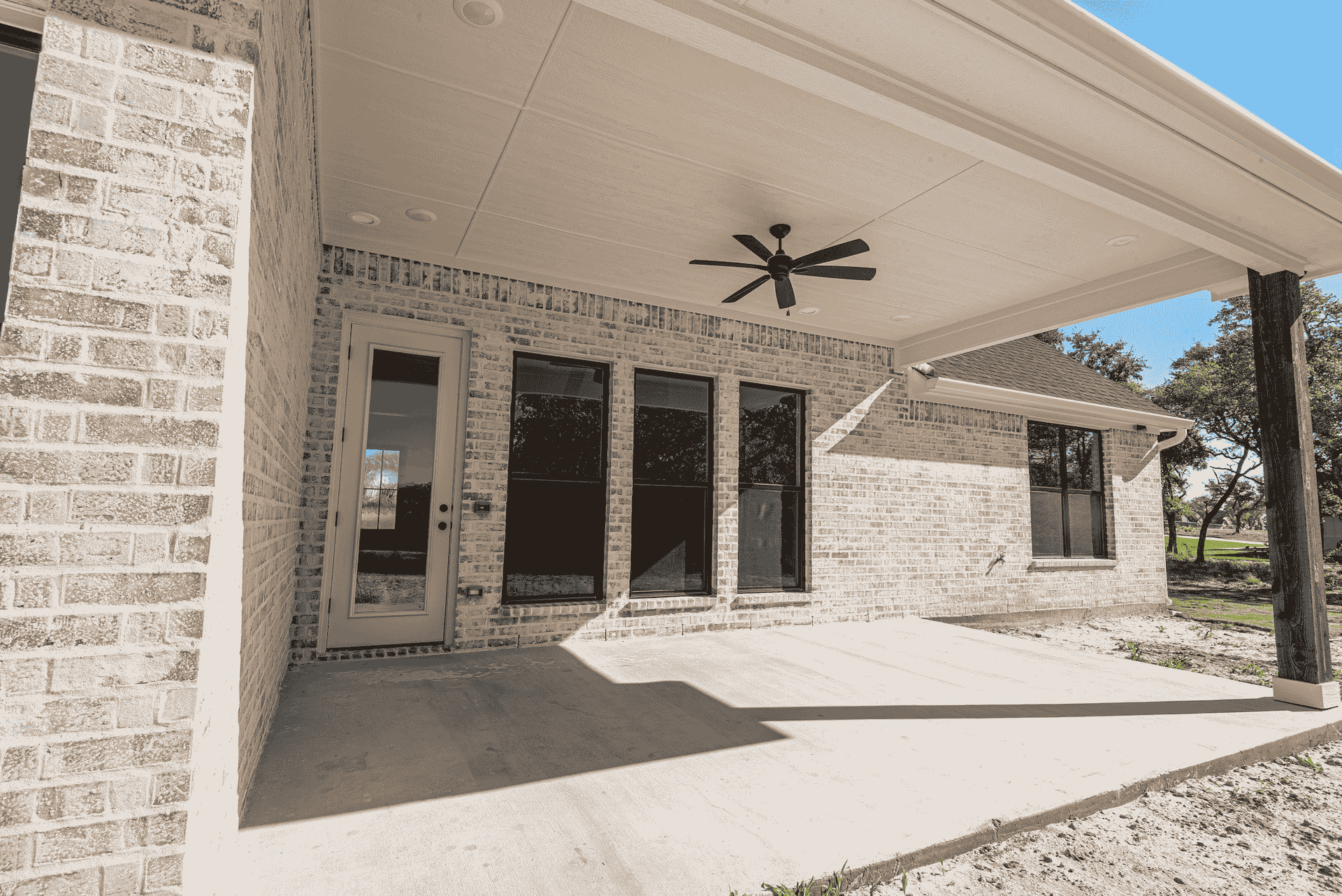 A white brick house with a covered patio and a ceiling fan.