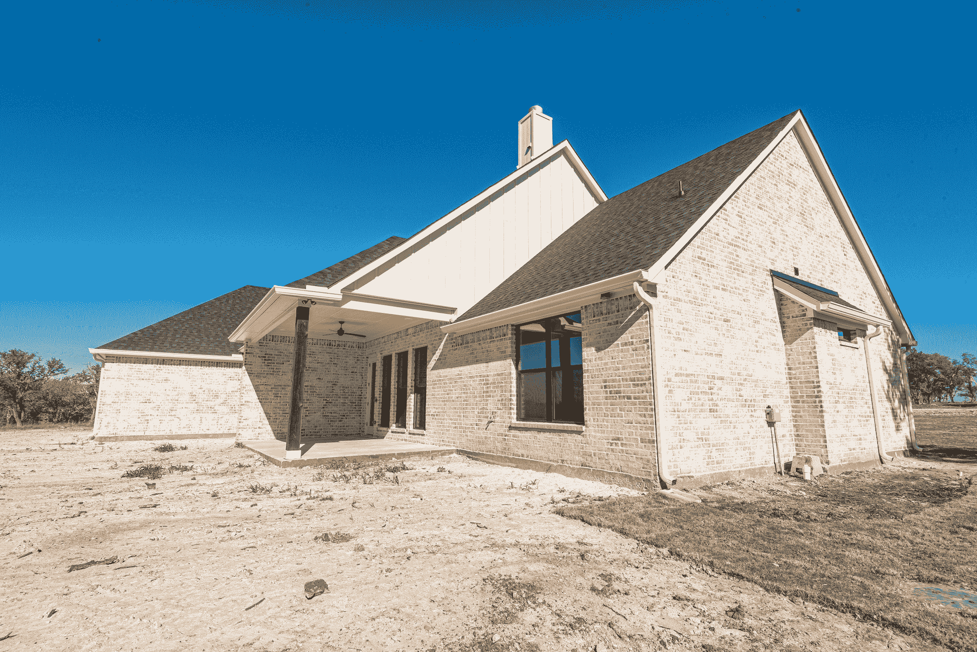 A white brick house with a black roof is sitting on top of a dirt field.