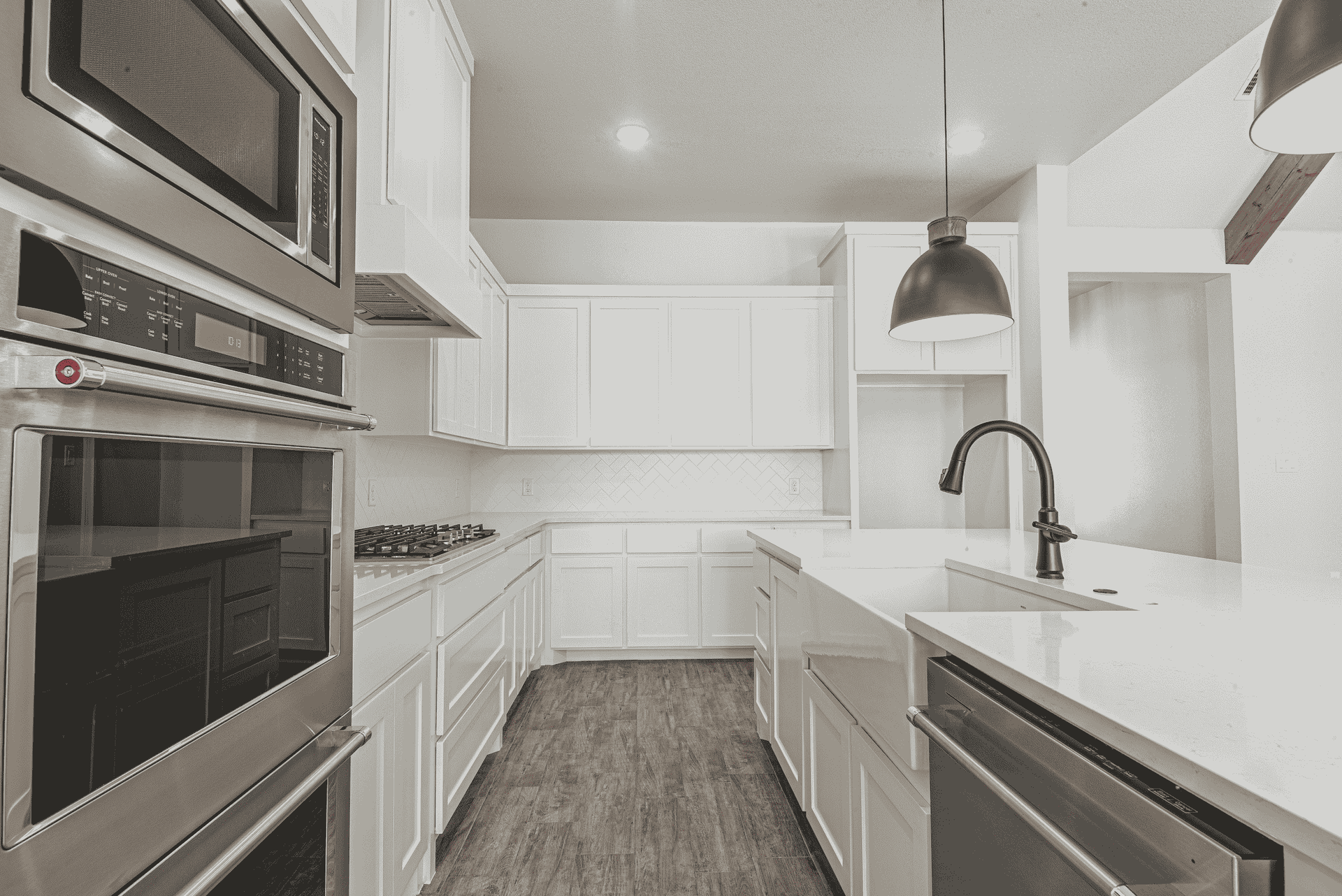 A black and white photo of a kitchen with white cabinets and stainless steel appliances.