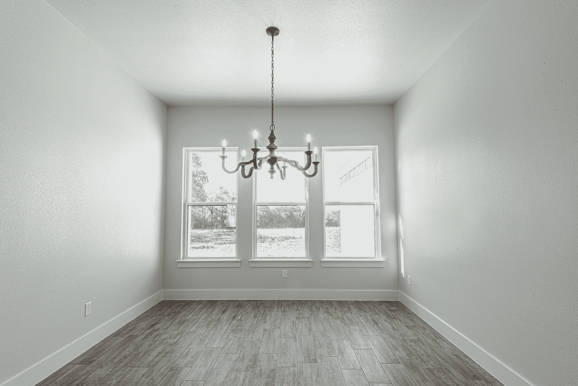 An empty room with a chandelier hanging from the ceiling and three windows.