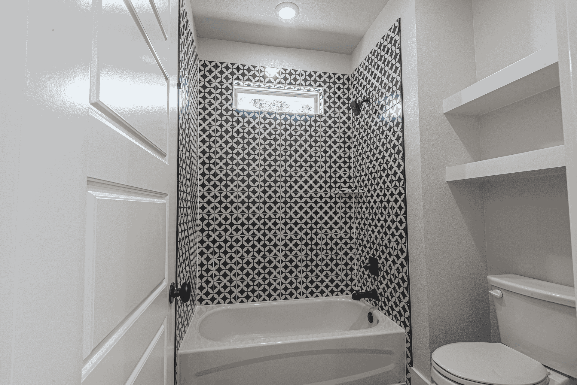 A bathroom with a bathtub , toilet , and shelves.