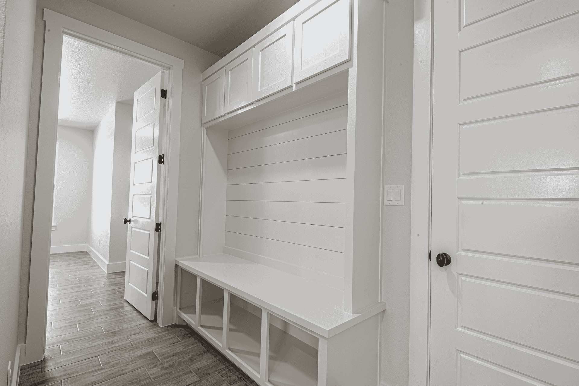 A black and white photo of a hallway with white cabinets and a bench.