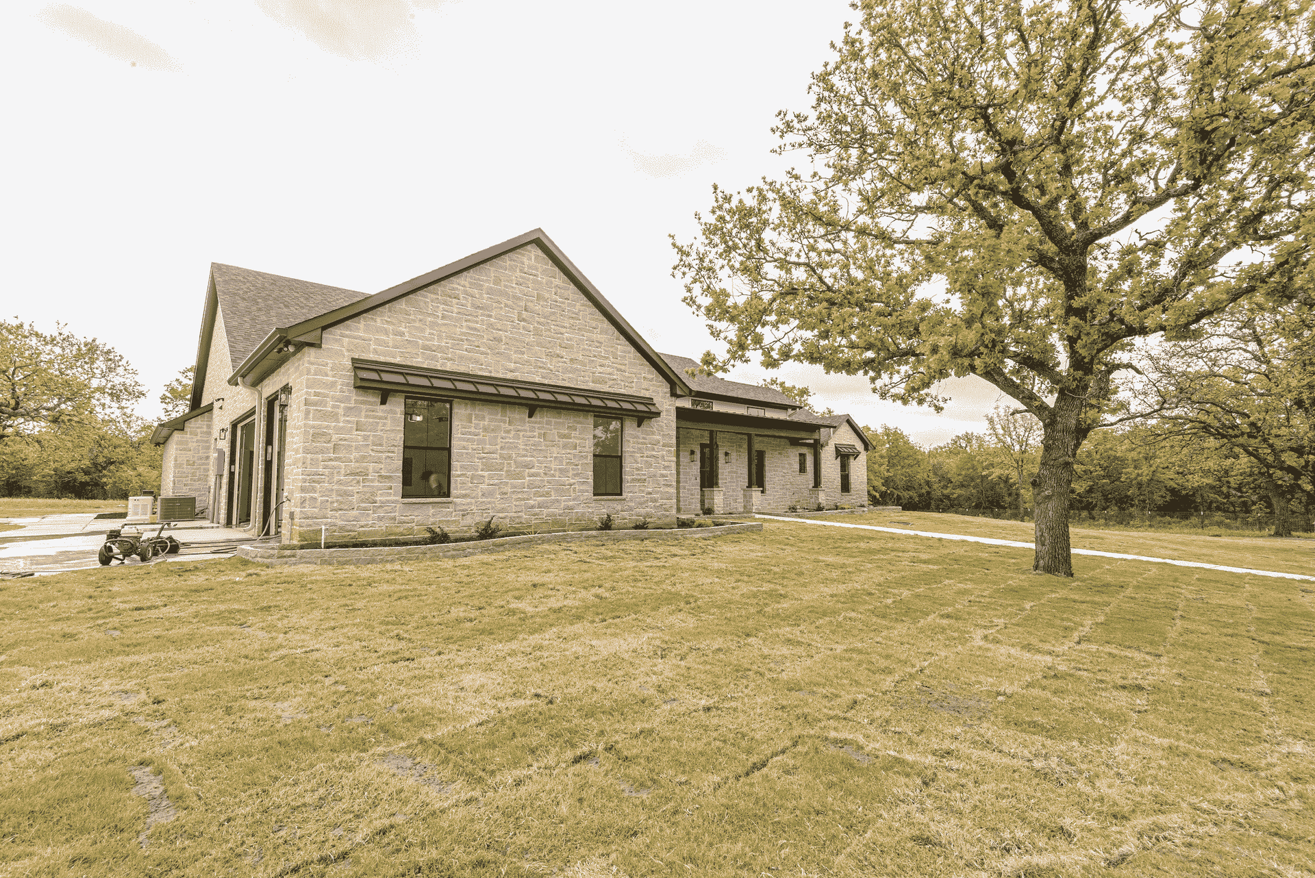 A brick house is sitting on top of a lush green field next to a tree.