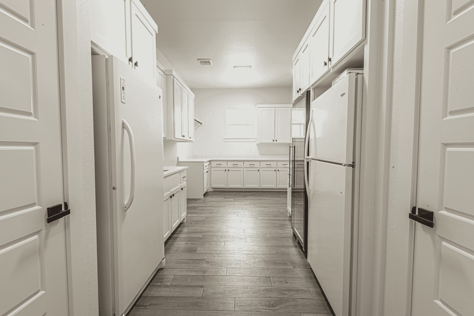 A long hallway leading to a kitchen with white cabinets and refrigerators.