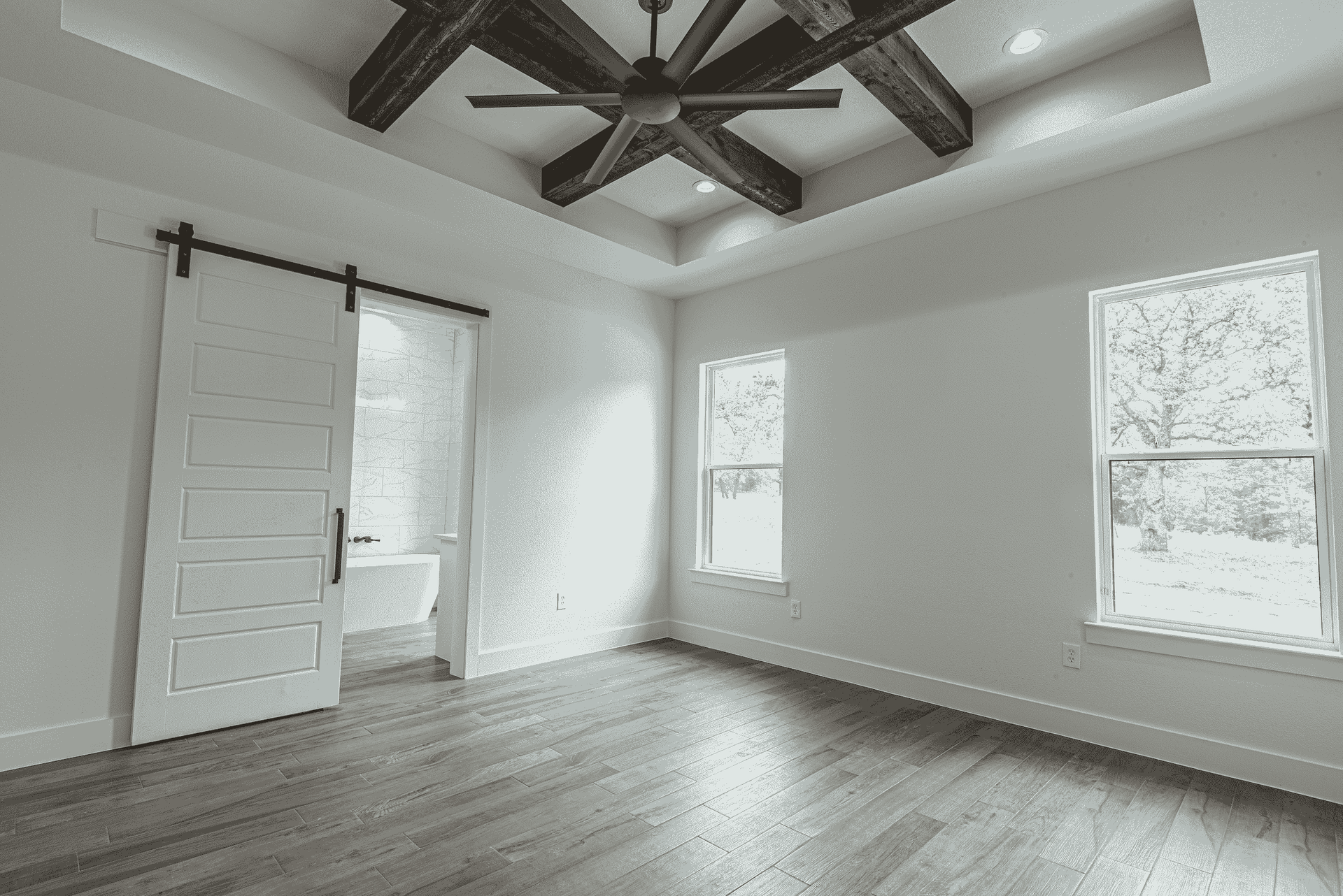 A black and white photo of an empty room with a ceiling fan and sliding barn door.