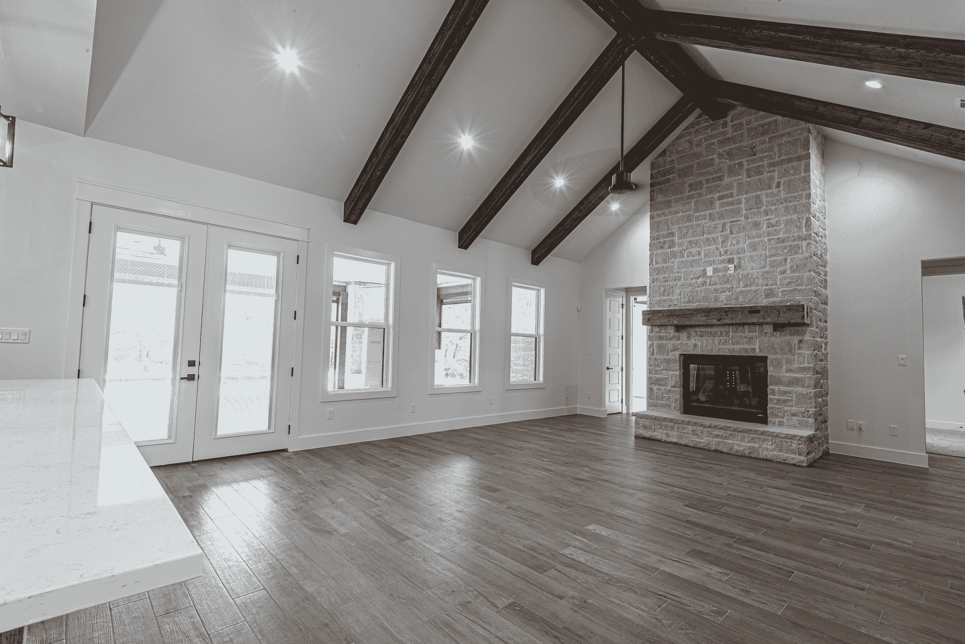 A black and white photo of an empty living room with hardwood floors and a fireplace.