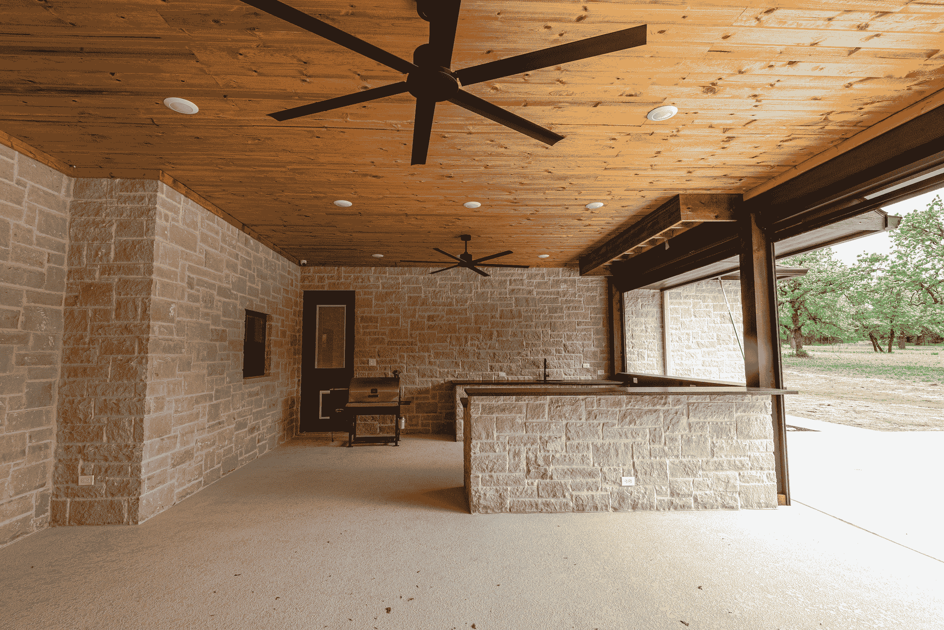 A large patio with a wooden ceiling and a ceiling fan.