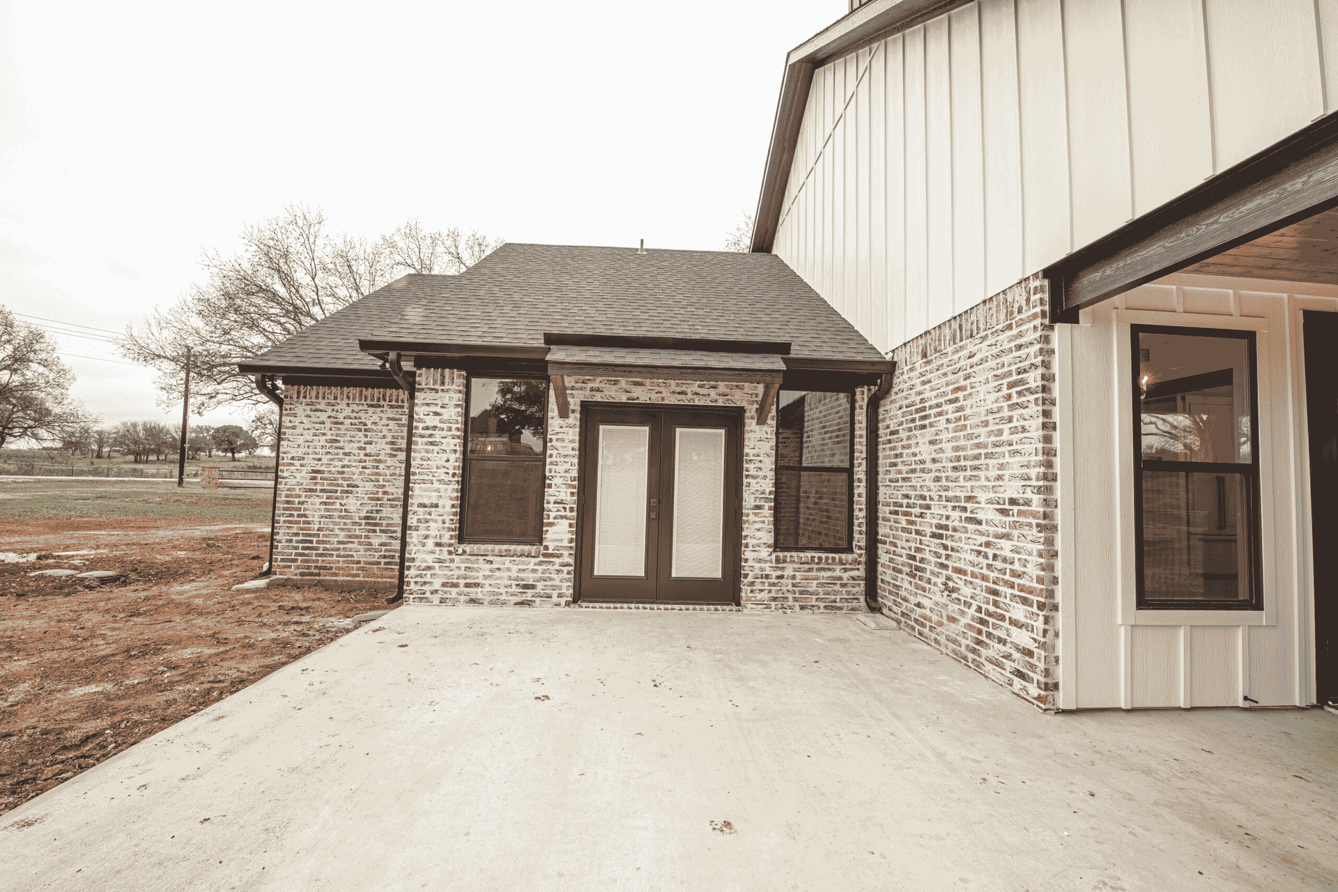 A black and white photo of a brick house with a concrete driveway leading to it.