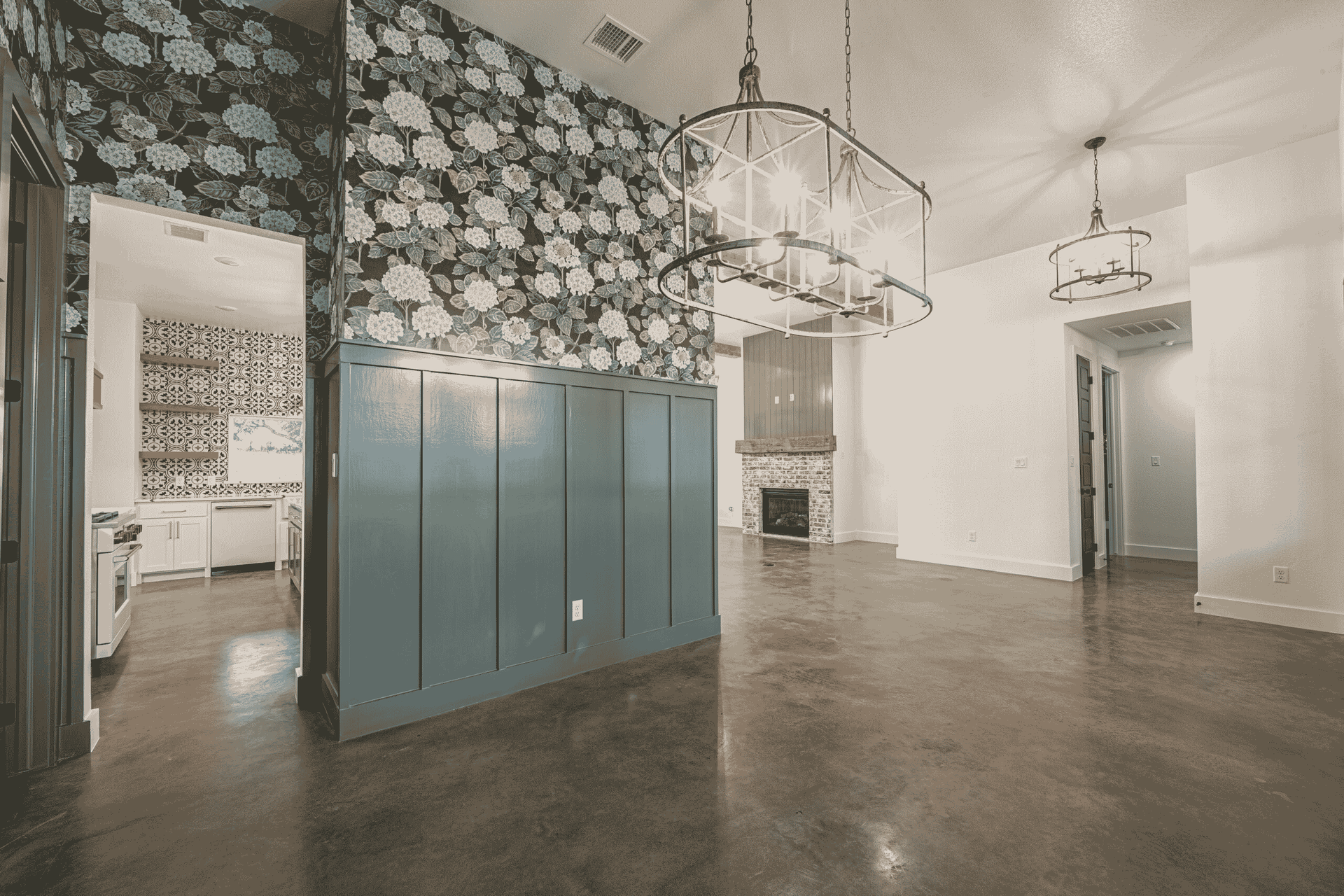 An empty room with a floral wallpaper on the wall and a chandelier hanging from the ceiling.