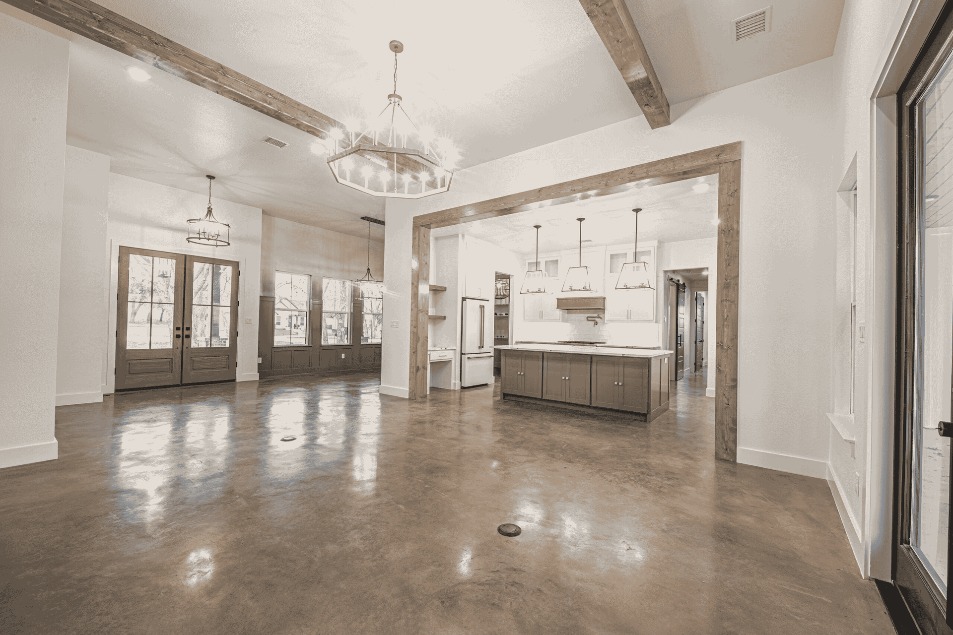 A large empty room with a kitchen and a chandelier.