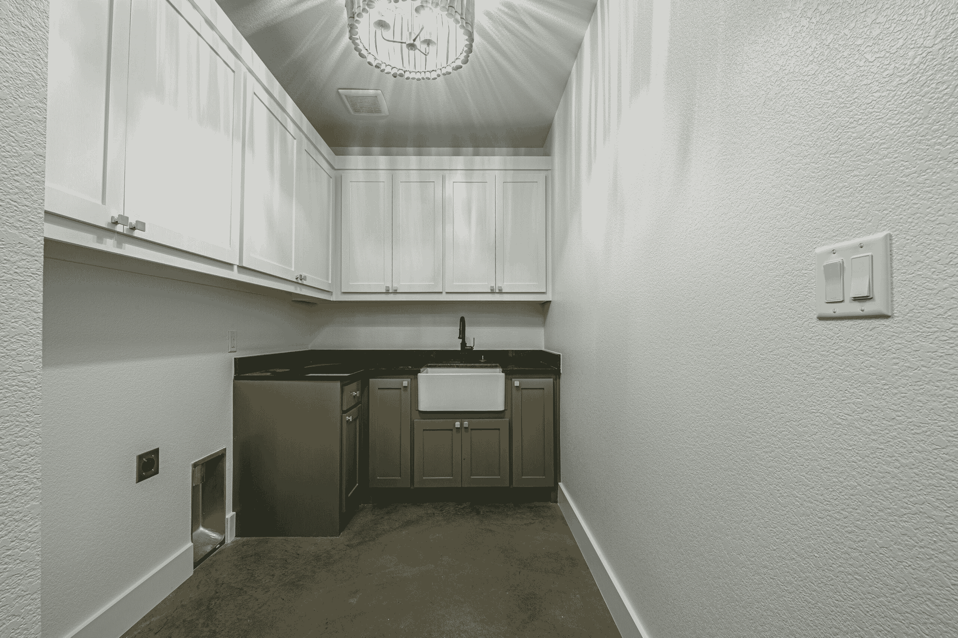 A black and white photo of a laundry room with a sink and cabinets.