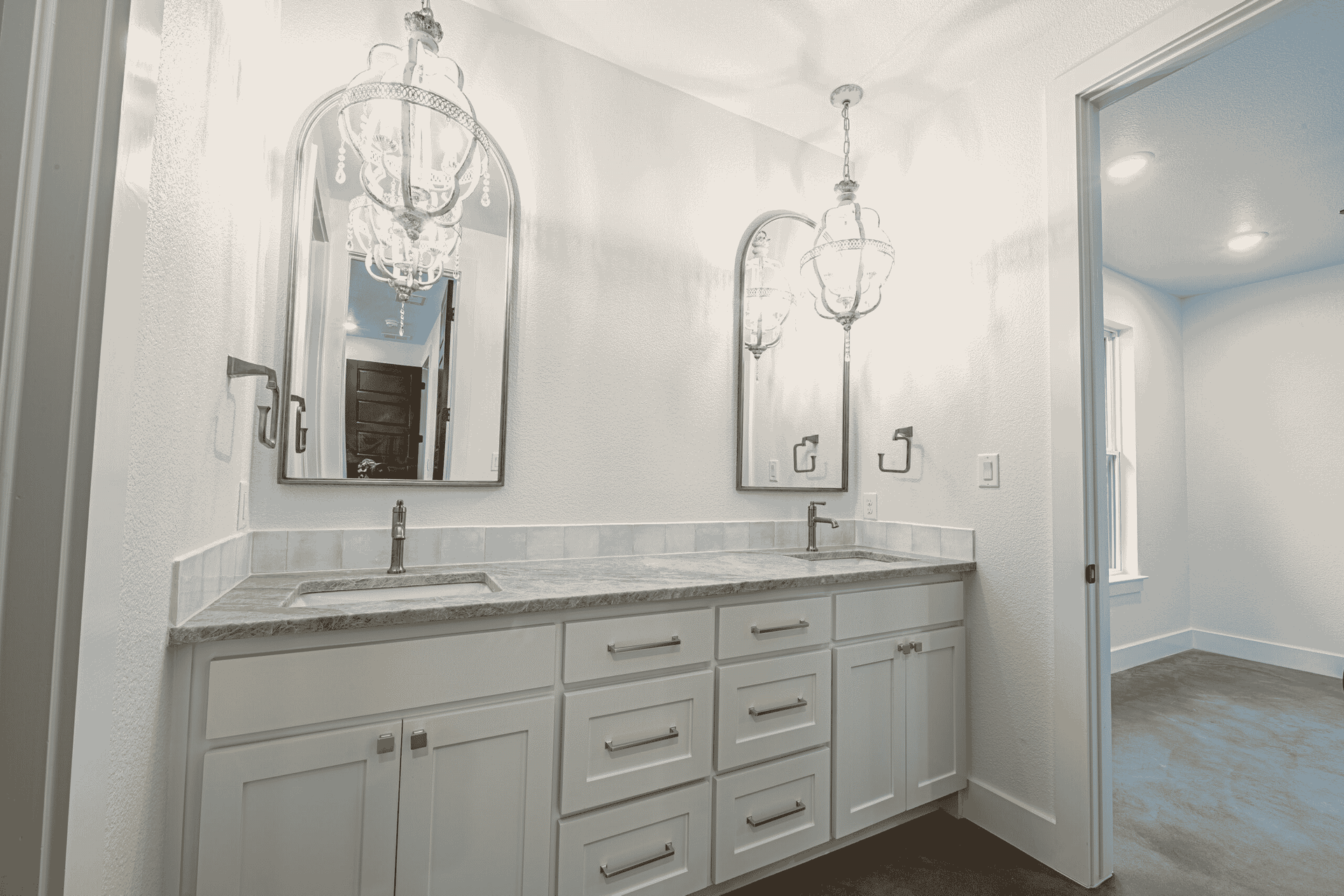 A bathroom with two sinks , two mirrors and a chandelier.