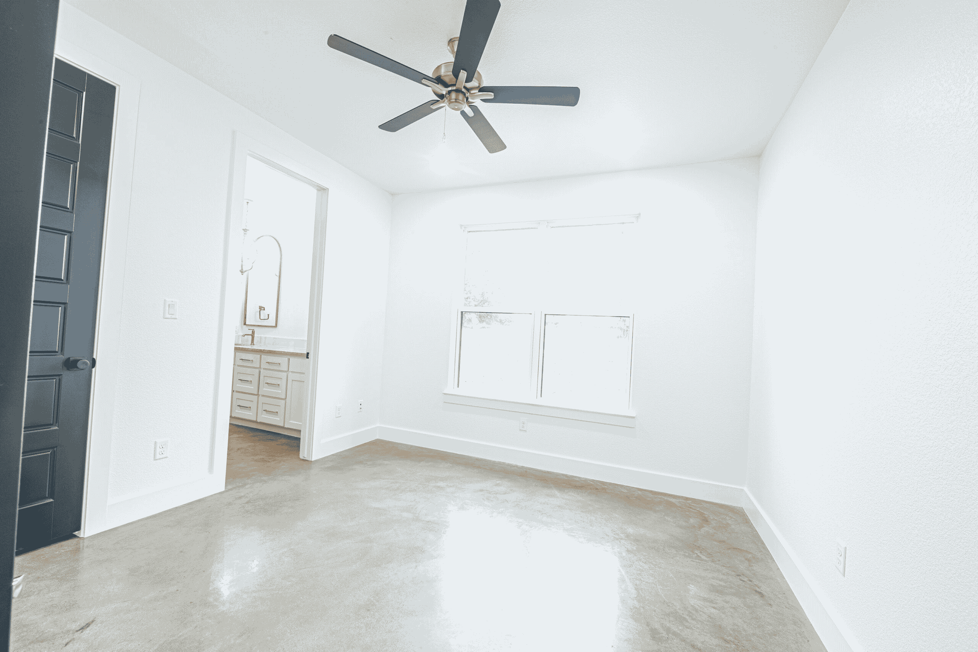 An empty room with a ceiling fan and two windows.