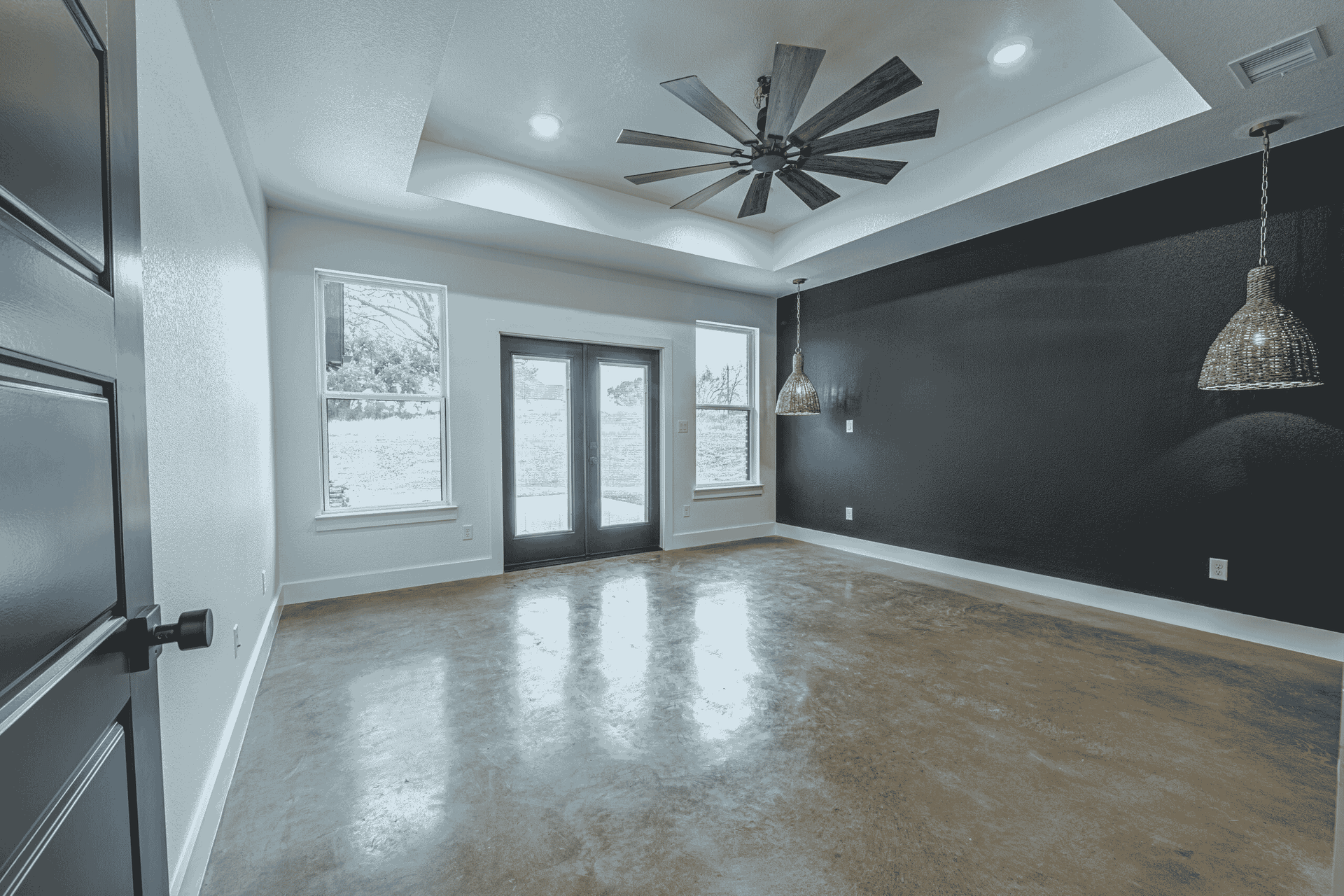 An empty living room with a ceiling fan and a black door.