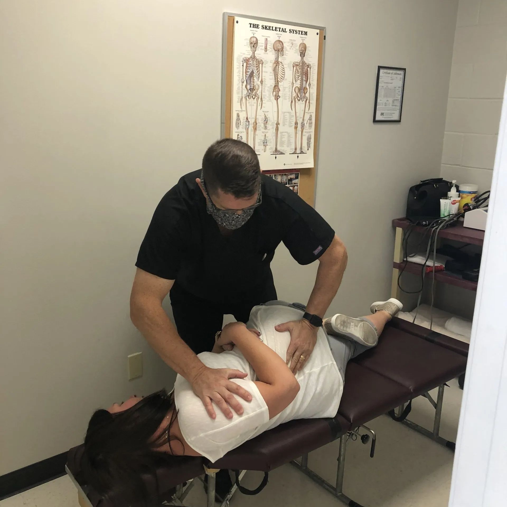Doctor adjusting a patient's back on an examination table in an office.
