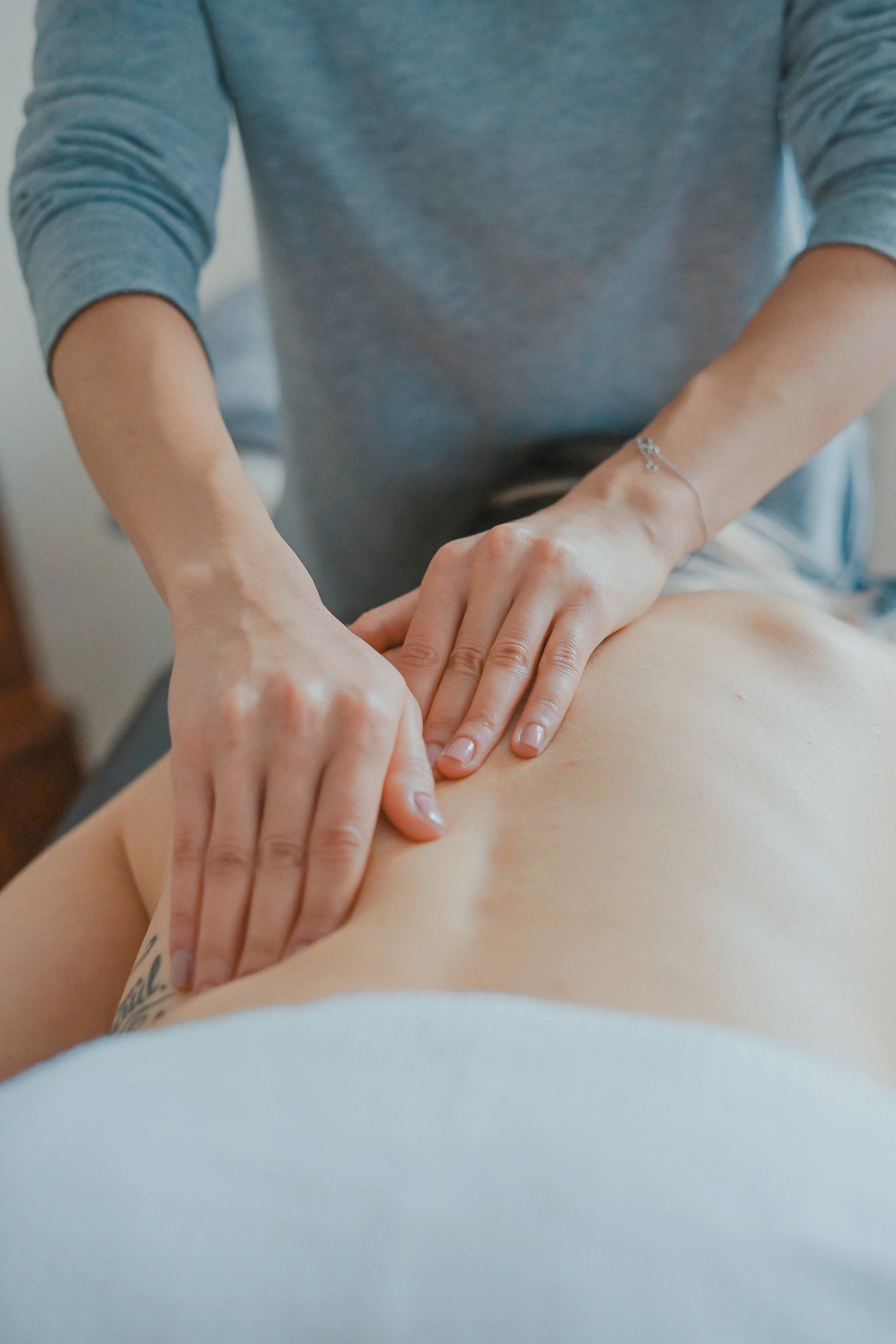 Hands massaging a person's back. Light skin, gray clothing, and soft lighting.