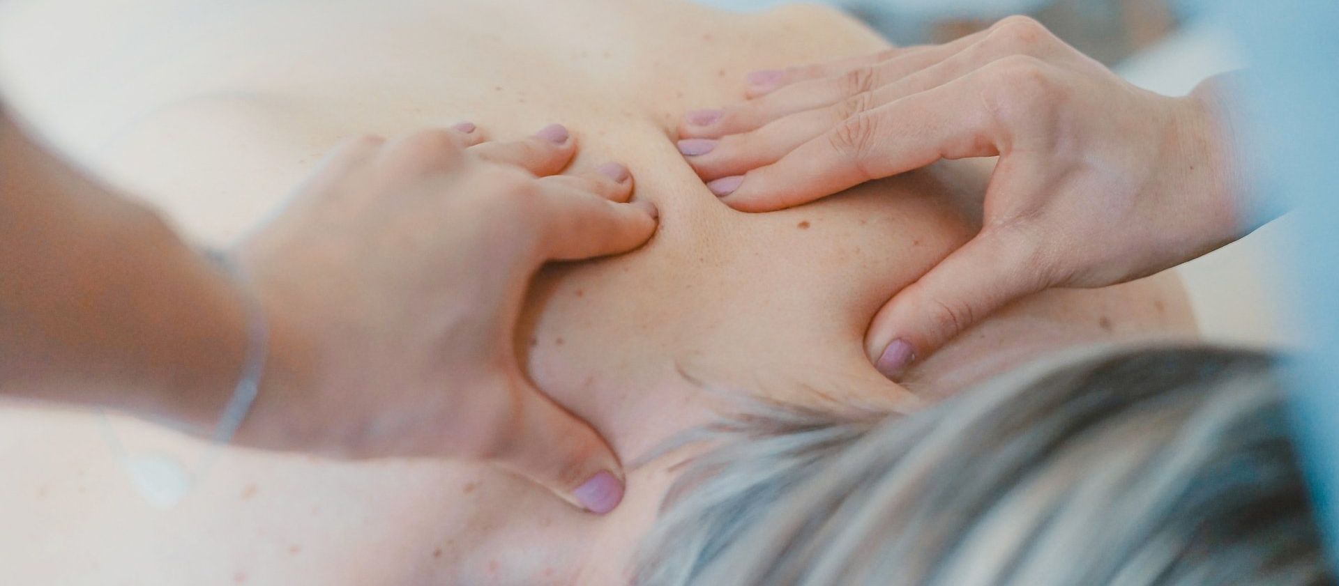 Hands massaging a person's shoulder and upper back.