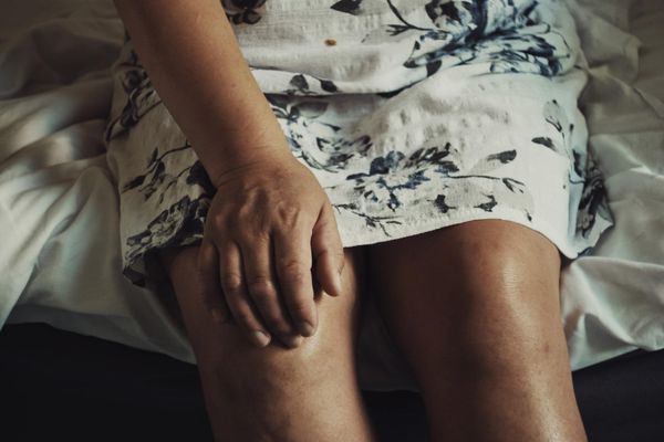 Person seated, hand on thigh. Floral print dress, visible legs, sitting on white sheets.