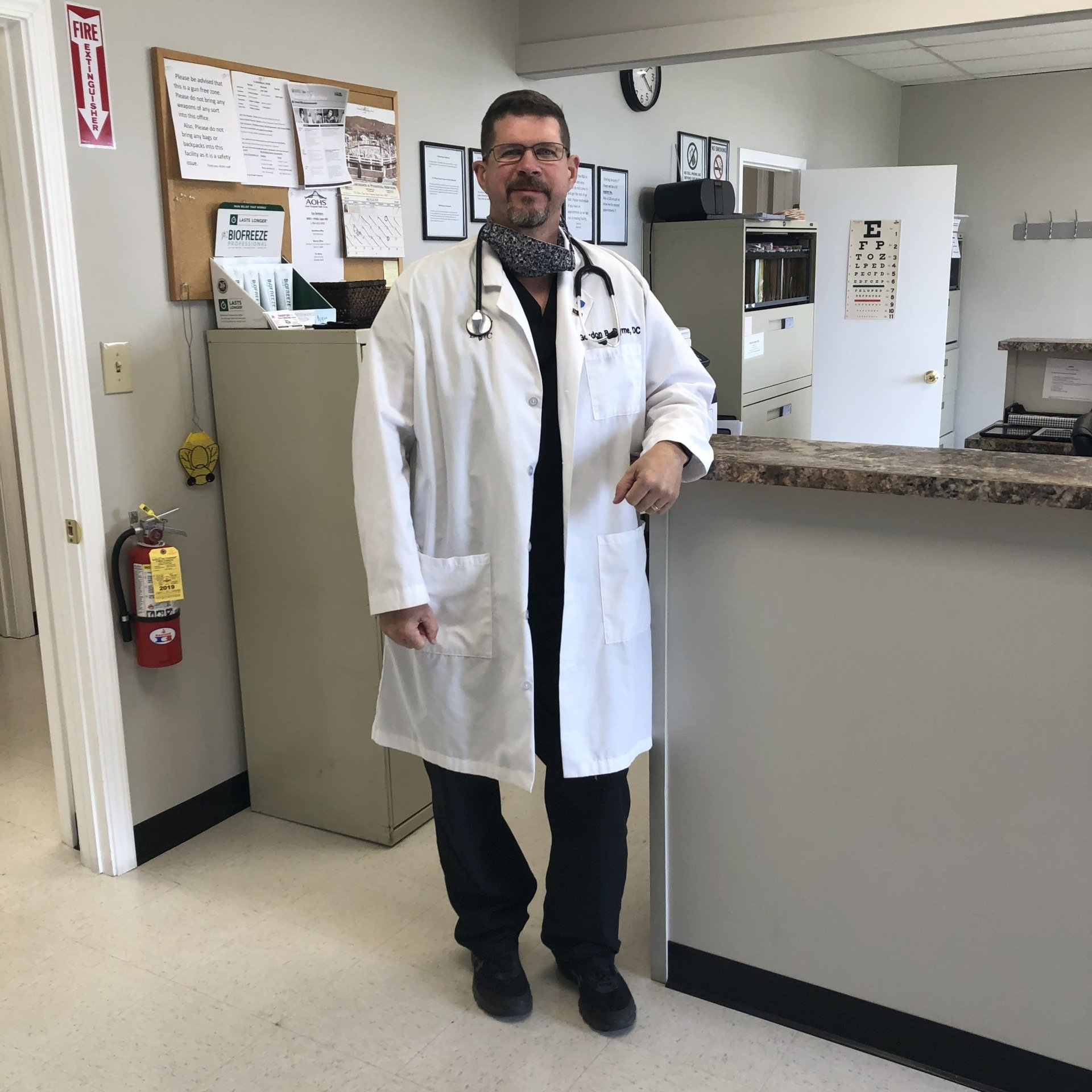 Doctor in white coat stands at a reception desk in a medical office.