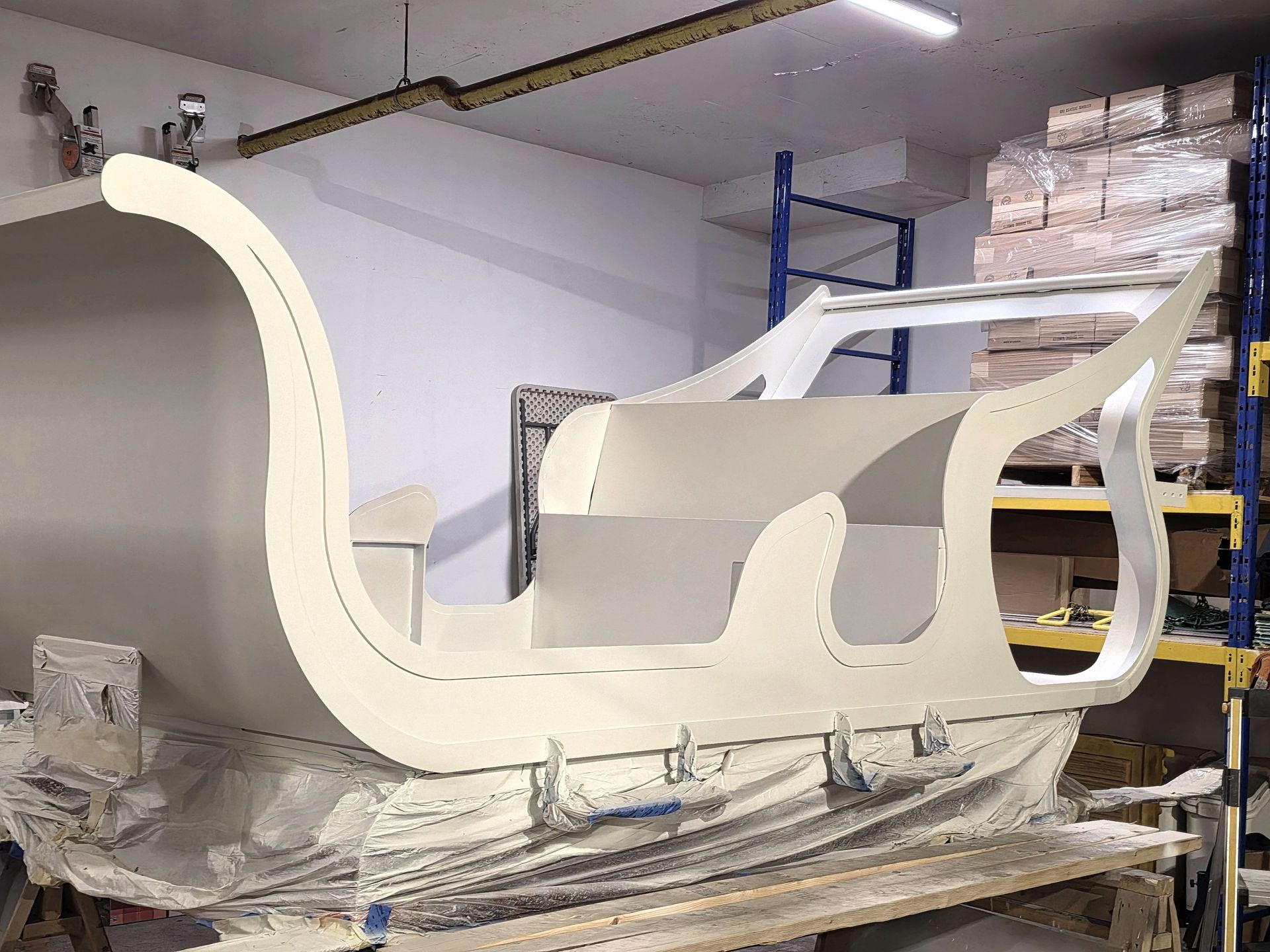 Canapé ou fauteuil blanc incurvé de style traîneau, emballé dans du plastique sur une palette, dans un atelier.