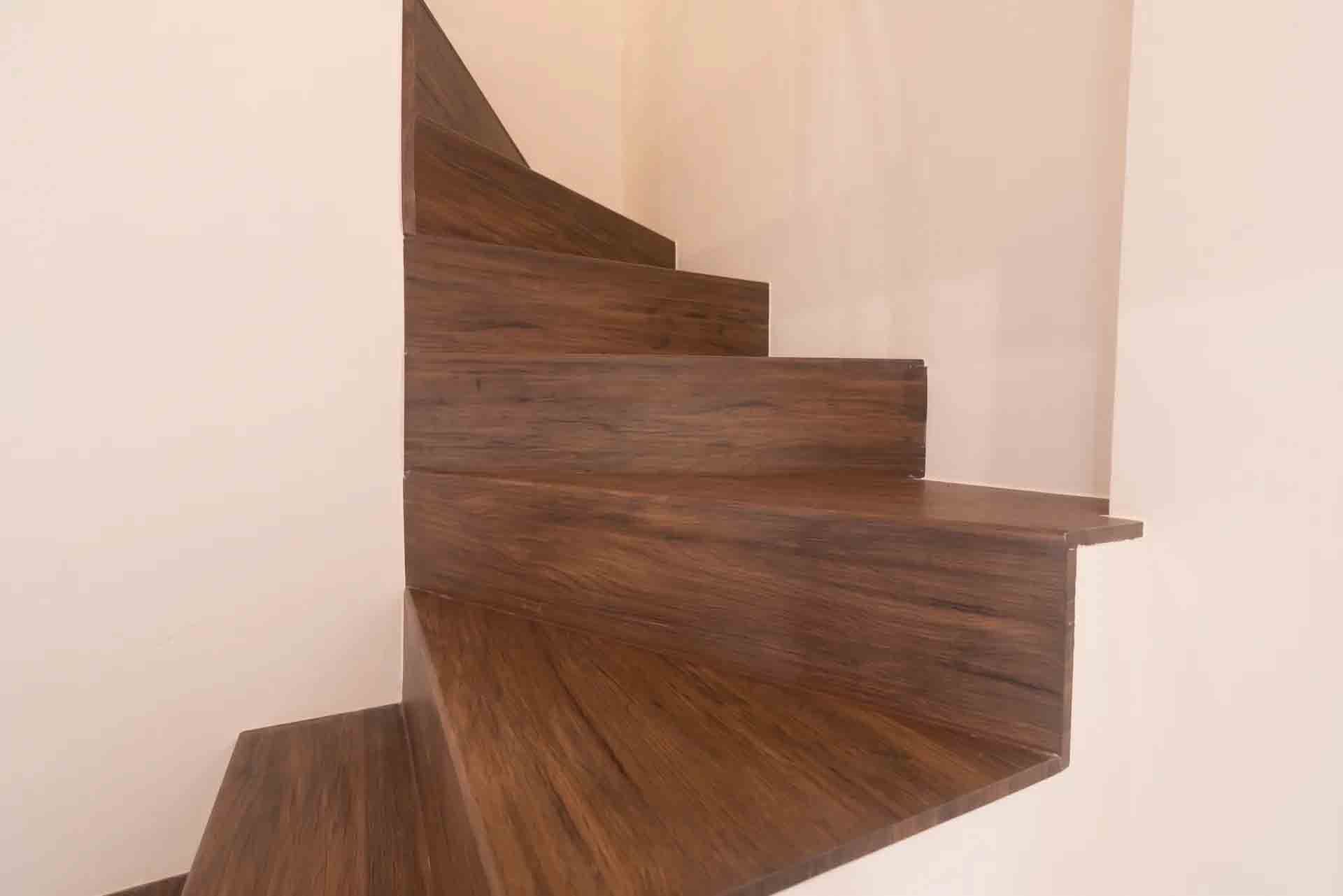 Escalier en bois courbé aux marches sombres, à côté d'un mur et d'un rideau de couleur claire