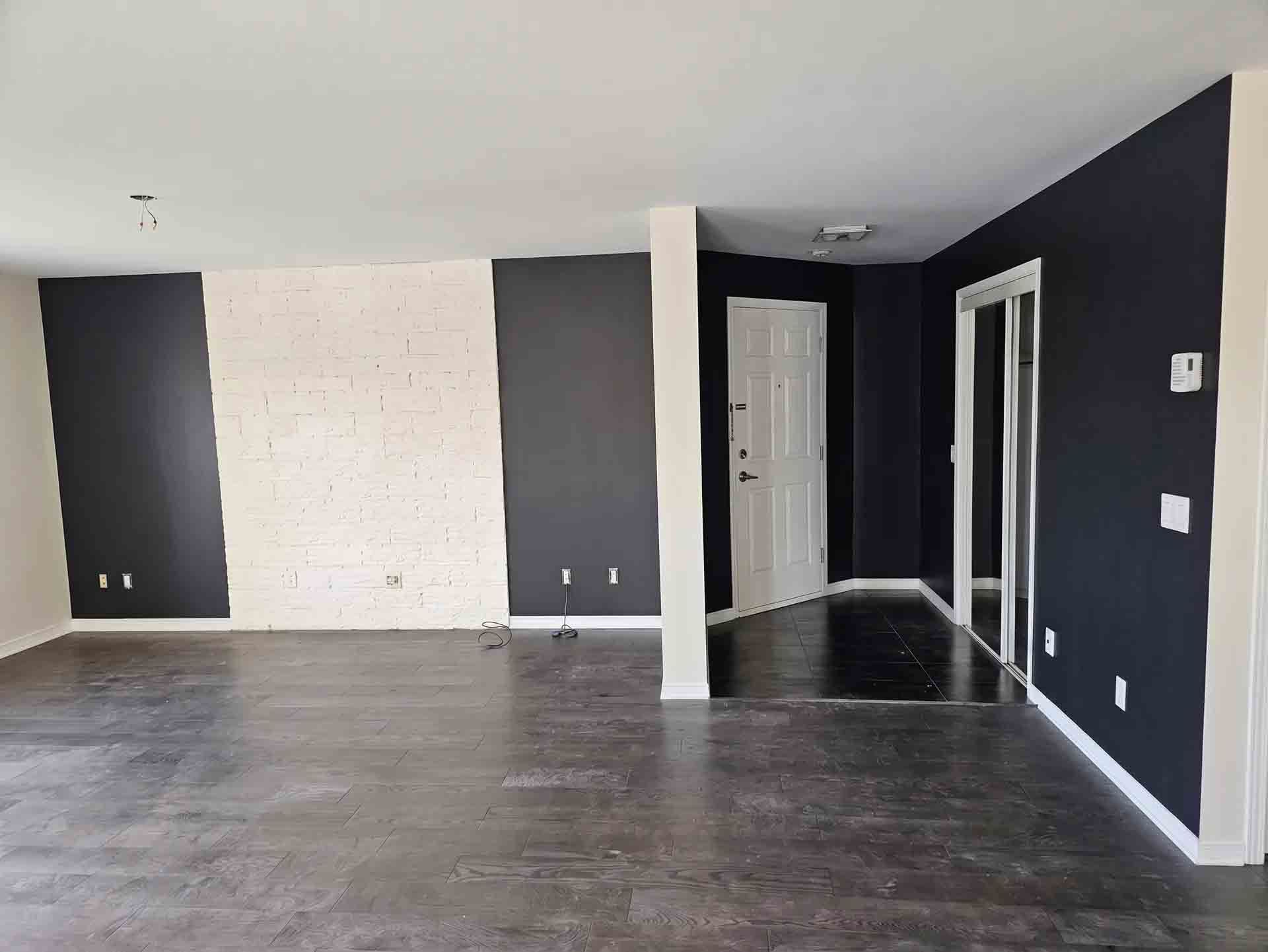 Salon moderne vide avec des murs d'accent sombres, une cheminée en briques blanches et un parquet gris.