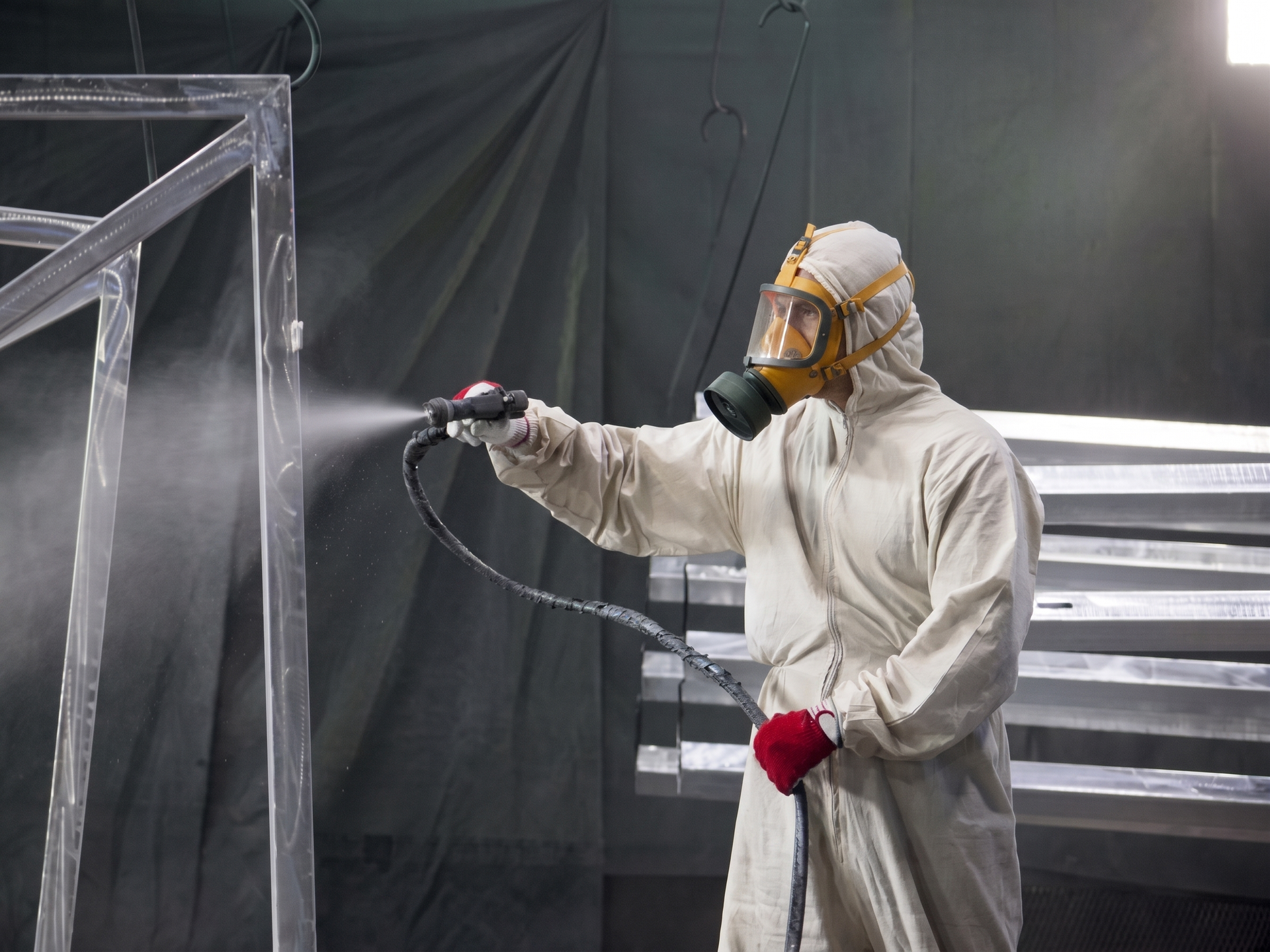 Personne en combinaison de protection pulvérisant un cadre métallique avec un pistolet à peinture