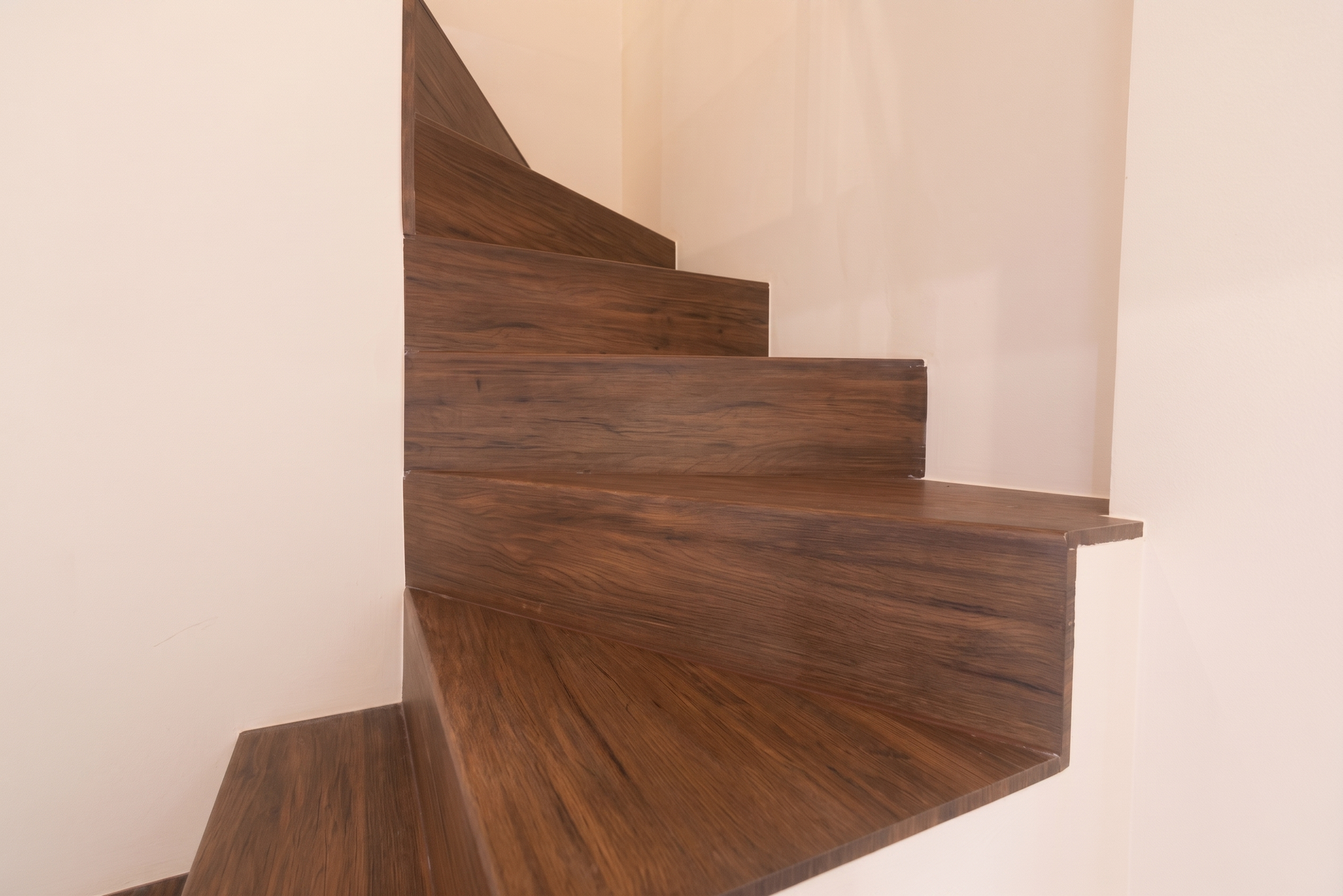 Escalier en bois courbé aux marches sombres, à côté d'un mur et d'un rideau de couleur claire