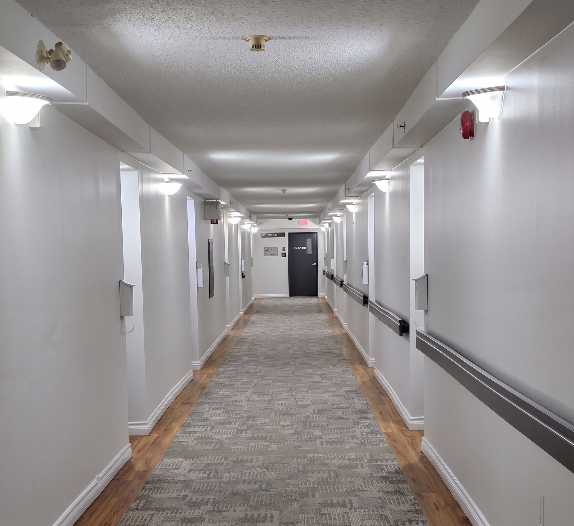 Couloir d'hôtel lumineux avec murs blancs, tapis de couloir, appliques murales et portes des deux côtés