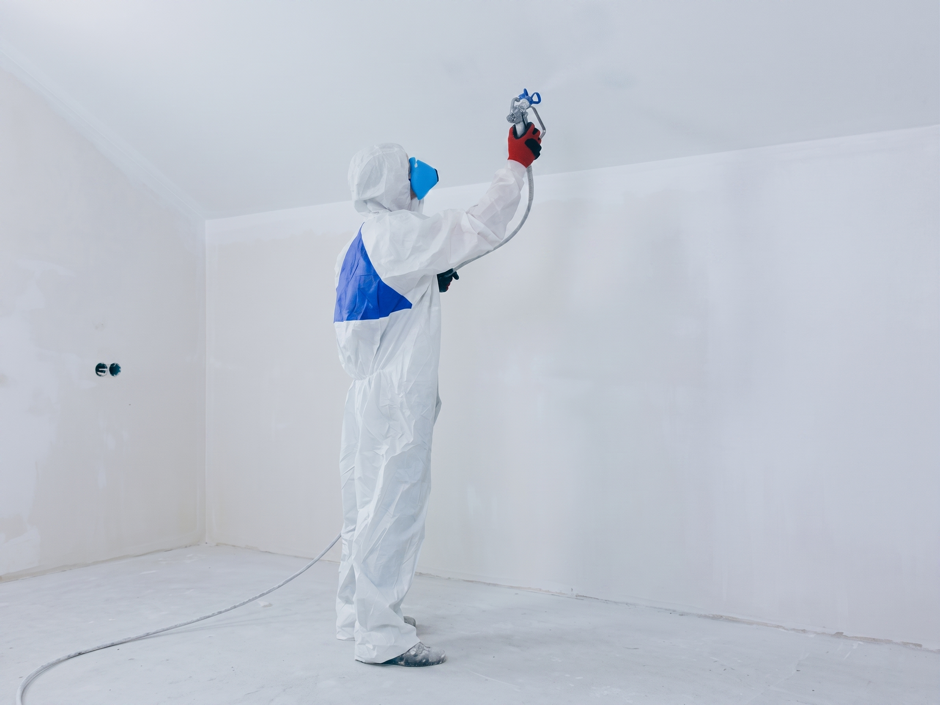 Une personne en combinaison de protection blanche peint à la bombe une pièce blanche avec un pistolet à peinture rouge.