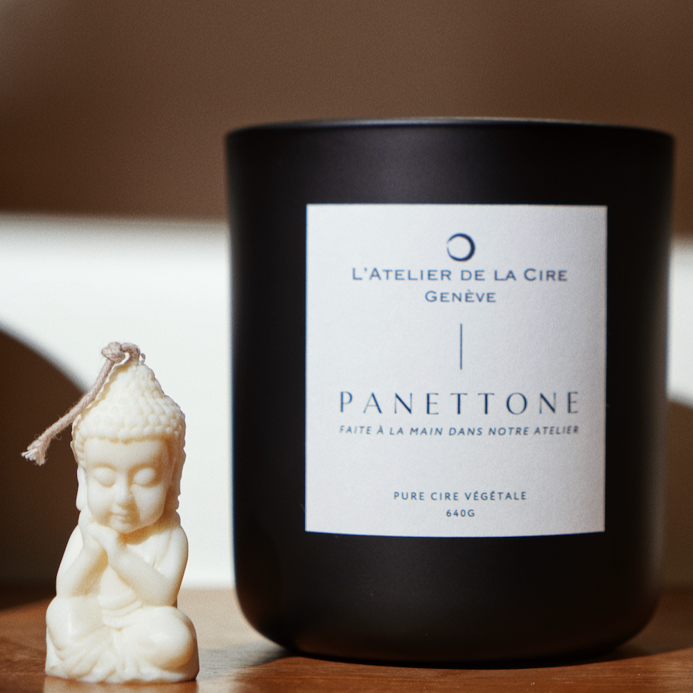 Bougie noire avec étiquette blanche et petite figurine de Bouddha sur surface en bois.