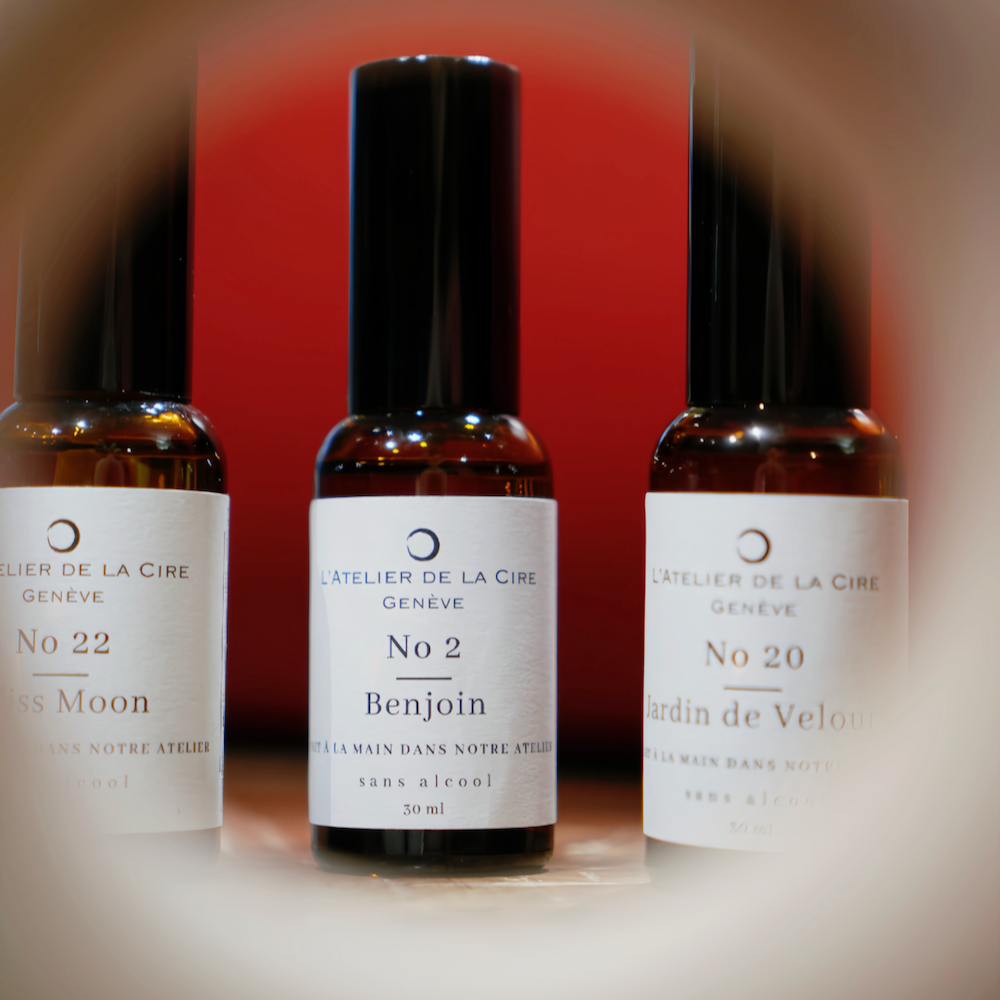 Trois flacons de parfum avec des étiquettes blanches, un liquide brun et des bouchons noirs, sur fond rouge.