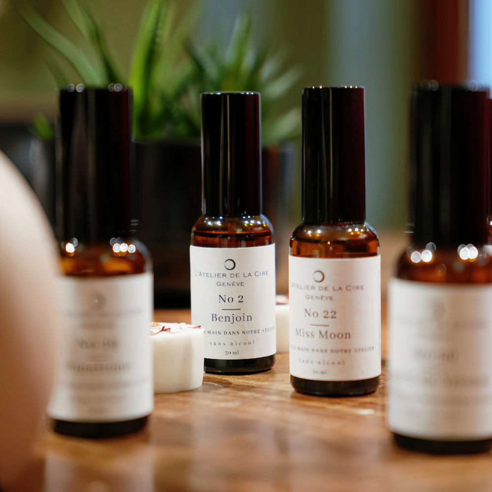 Trois flacons de parfum avec des étiquettes blanches, un liquide brun et des bouchons noirs, sur fond rouge.