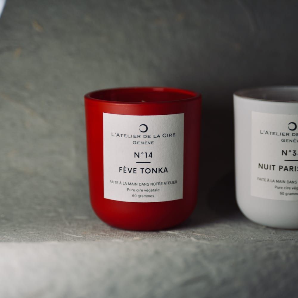 Deux bougies, rouge et blanche, avec étiquettes. La bougie rouge porte l'inscription « Fève Tonka » et la bougie blanche « Nuit Paris ».