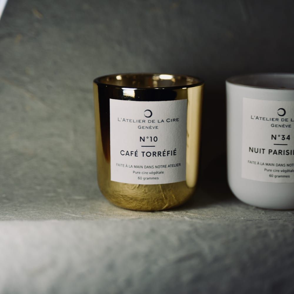 Deux bougies, rouge et blanche, avec étiquettes. La bougie rouge porte l'inscription « Fève Tonka » et la bougie blanche « Nuit Paris ».