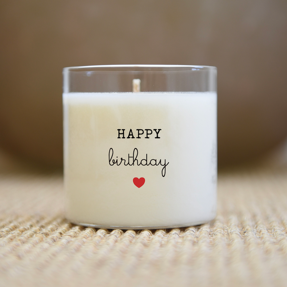 Bougie avec le texte « Joyeux anniversaire » et un cœur rouge, posée sur une surface texturée.