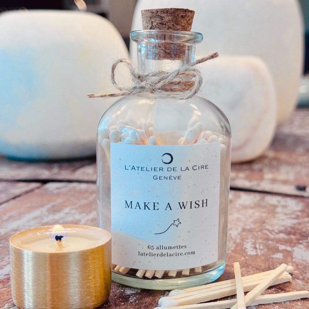 Bouteille en verre d'allumettes étiquetée « Make a Wish » avec bouchon, nœud et bougie allumée.