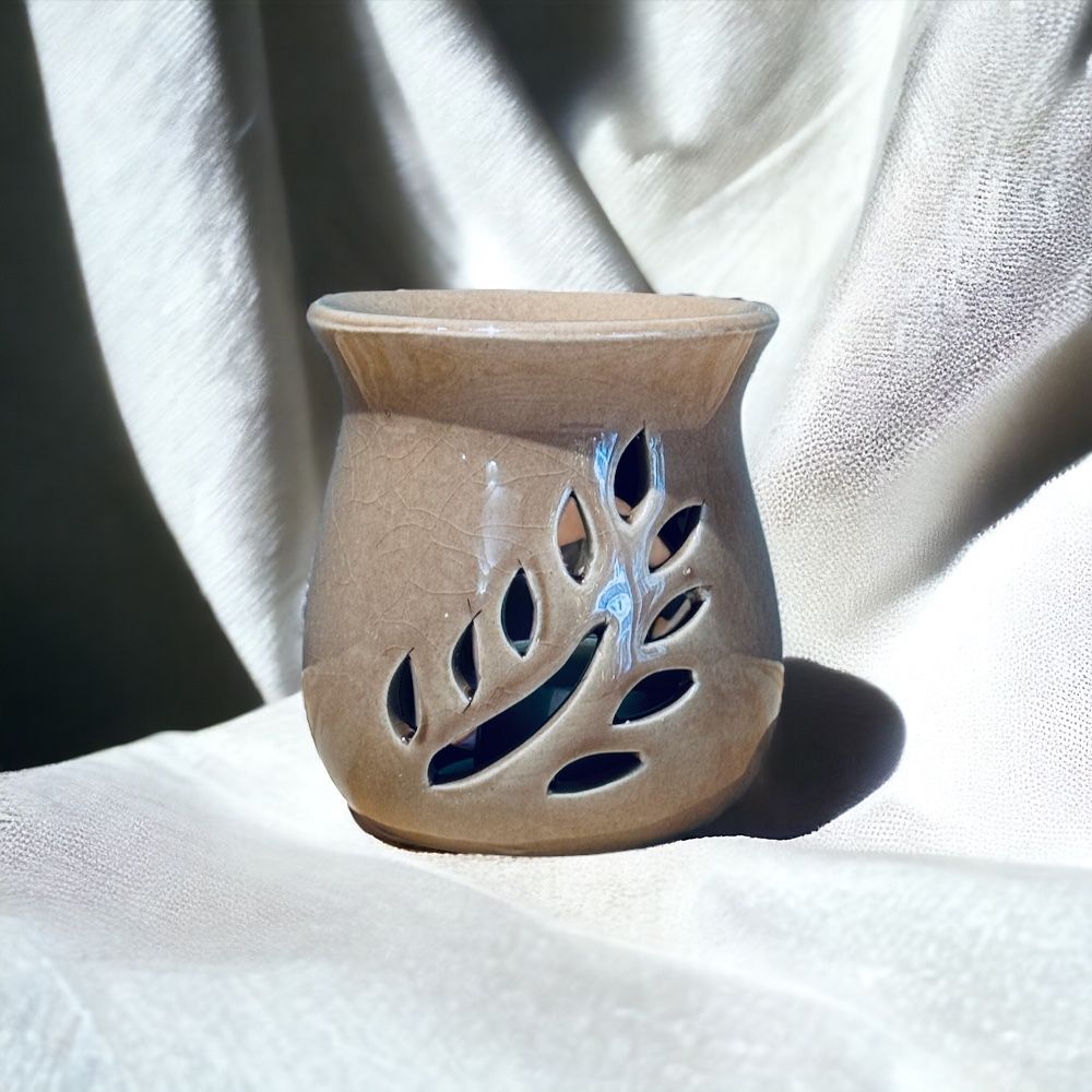 Diffuseur d'huiles essentielles en céramique beige avec découpes en forme de feuille, posé sur un tissu blanc cassé texturé.