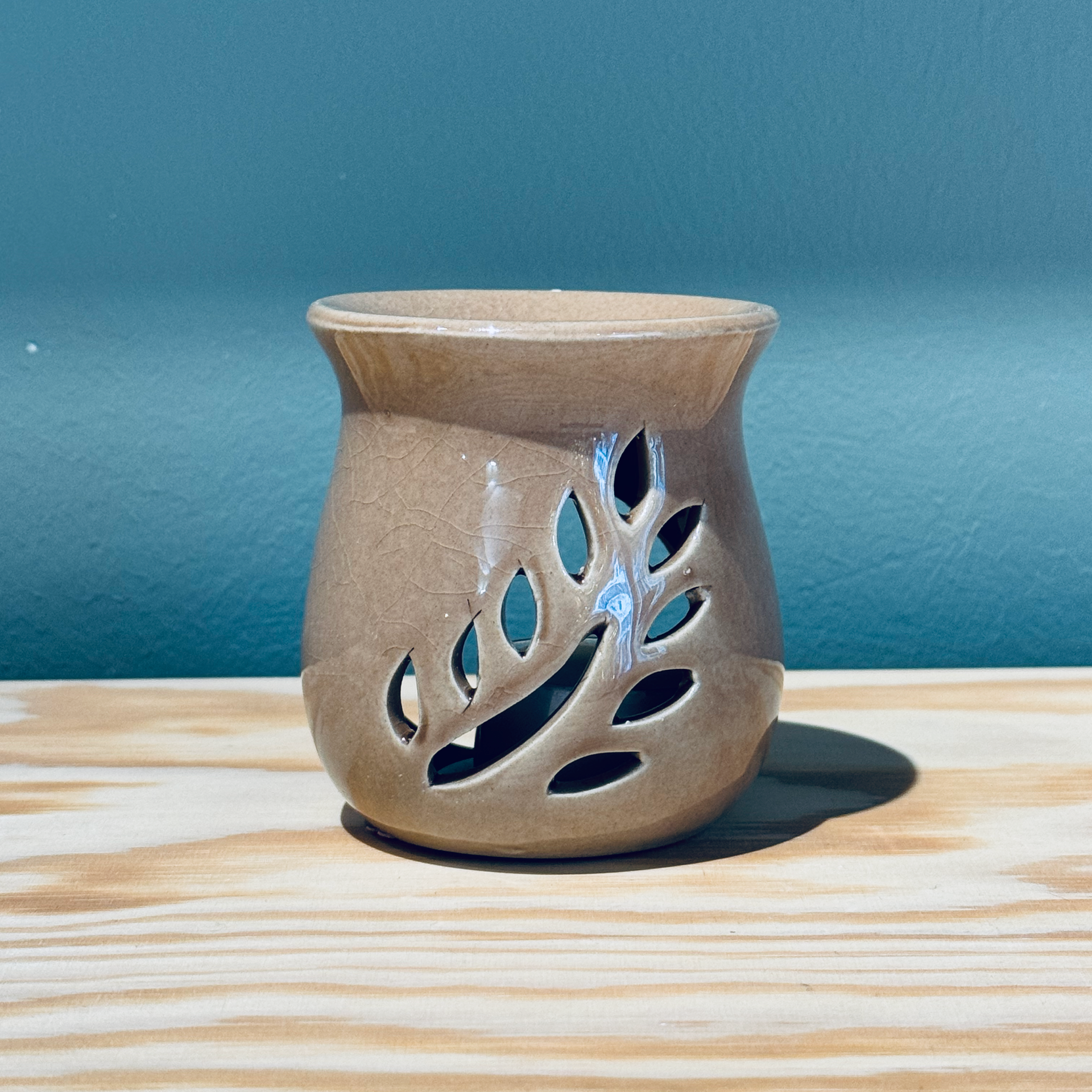 Diffuseur d'huiles essentielles en céramique beige avec découpes en forme de feuille, posé sur un tissu blanc cassé texturé.