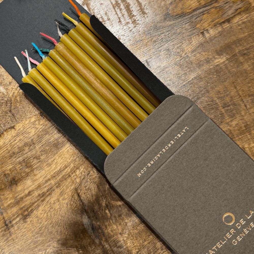 Bougies en cire d'abeille de différentes tailles avec mèches colorées, dans un sac en papier avec des papiers.