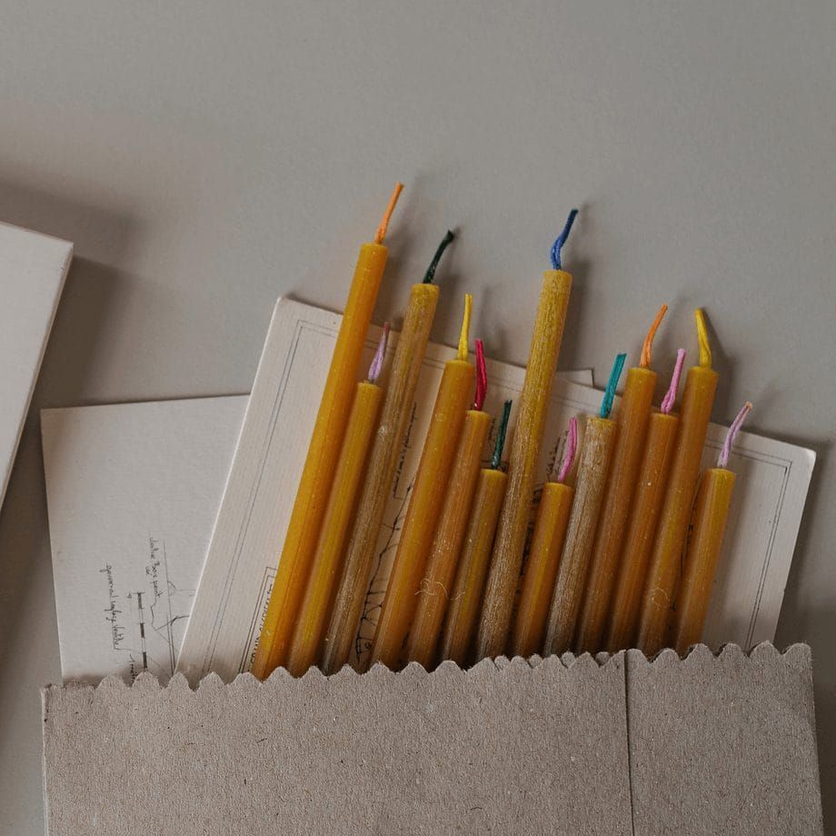 Bougies en cire d'abeille de différentes tailles avec mèches colorées, dans un sac en papier avec des papiers.