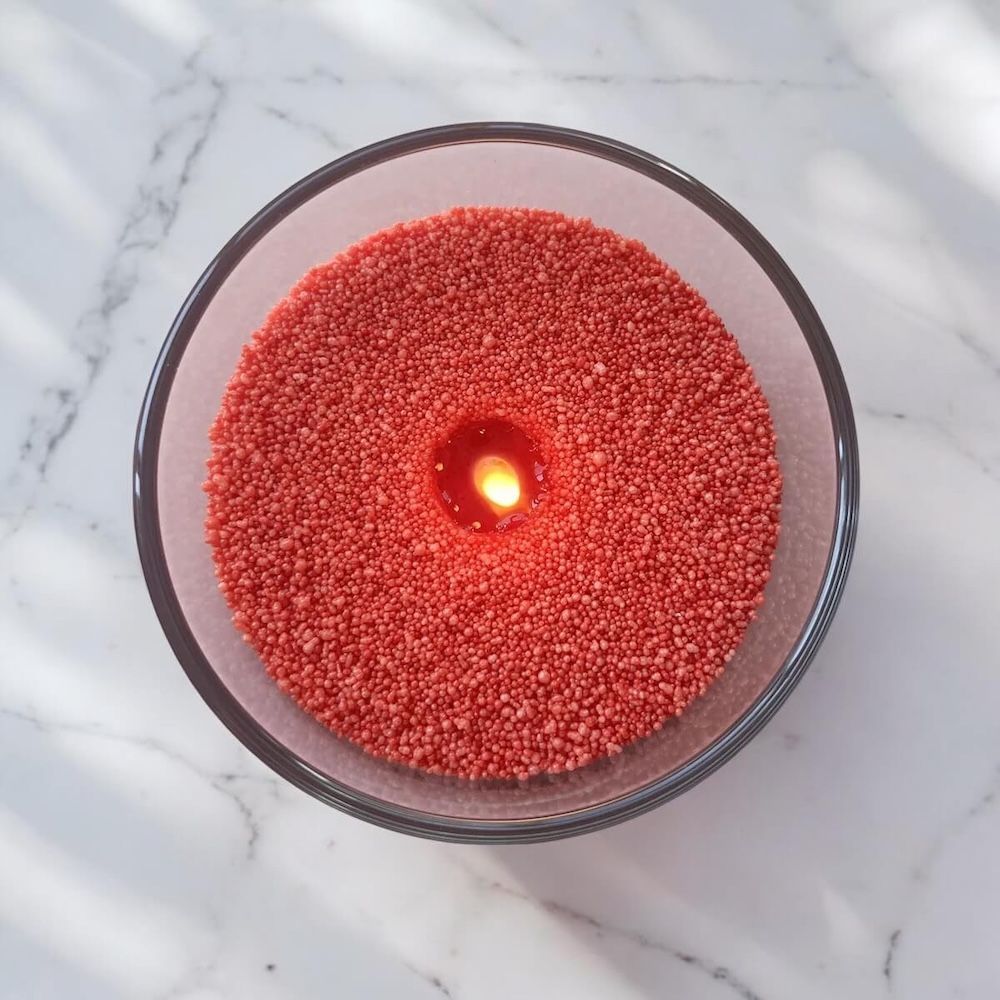 Bougie rouge allumée dans un bol en verre transparent, sur une surface en marbre, vue aérienne.