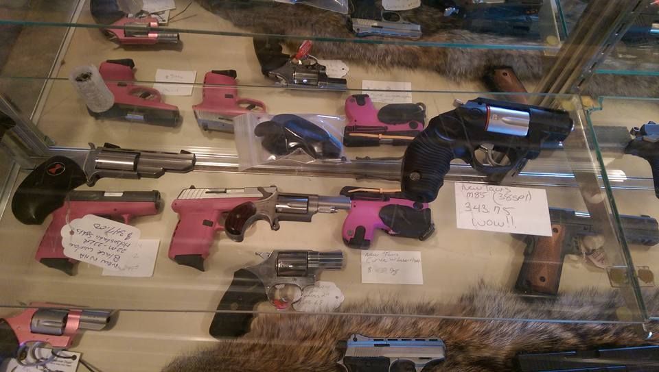 Display case with various handguns, some with pink accents, in a gun store.