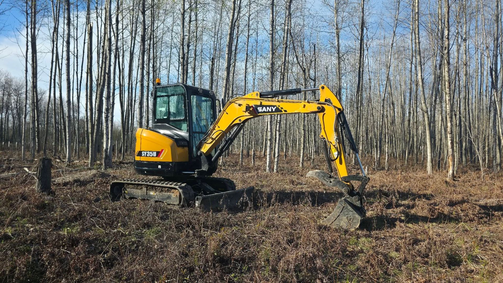 Yellow excavator digging in a field with leafless trees in the background