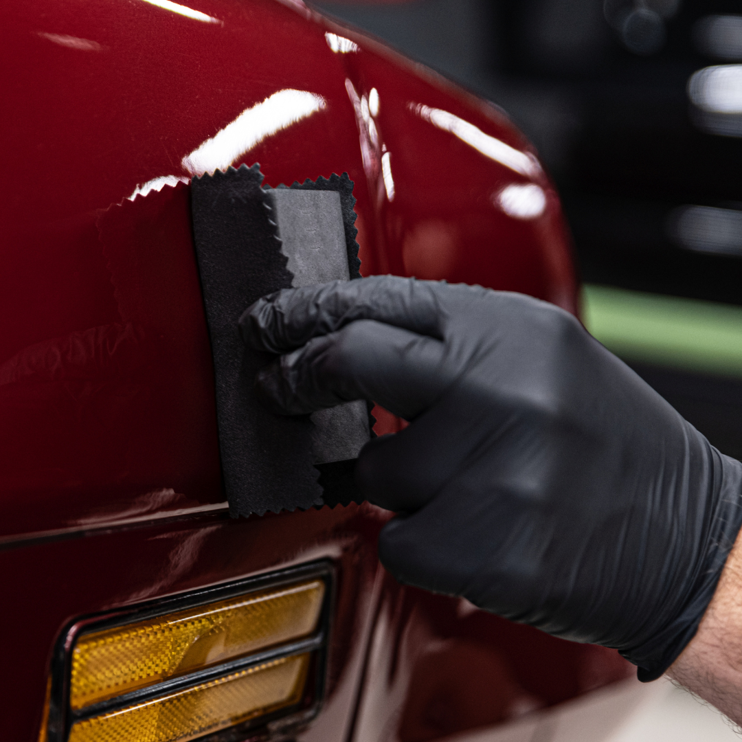 A person wearing black gloves is polishing a red car