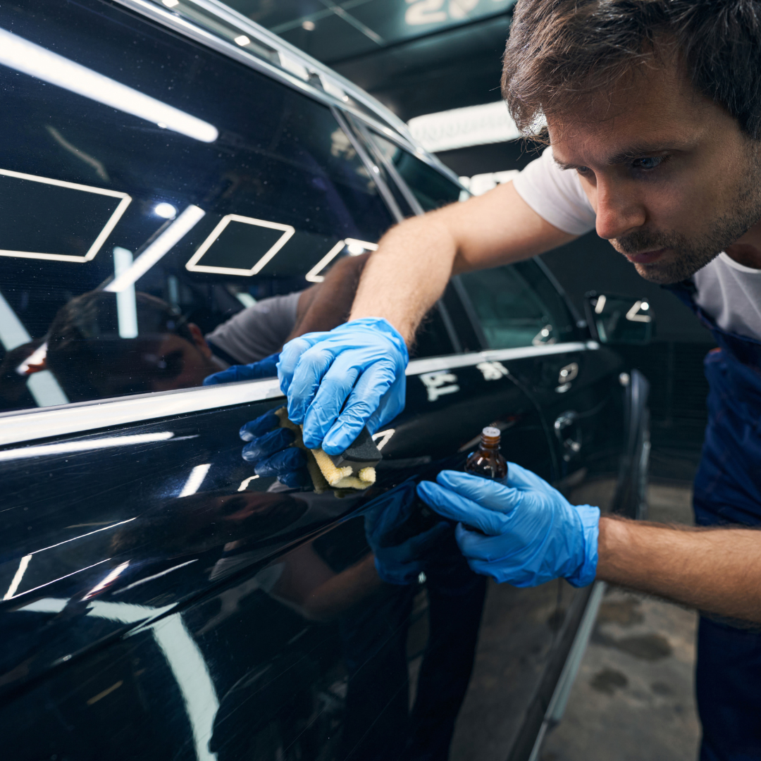 A man wearing blue gloves is polishing a car door