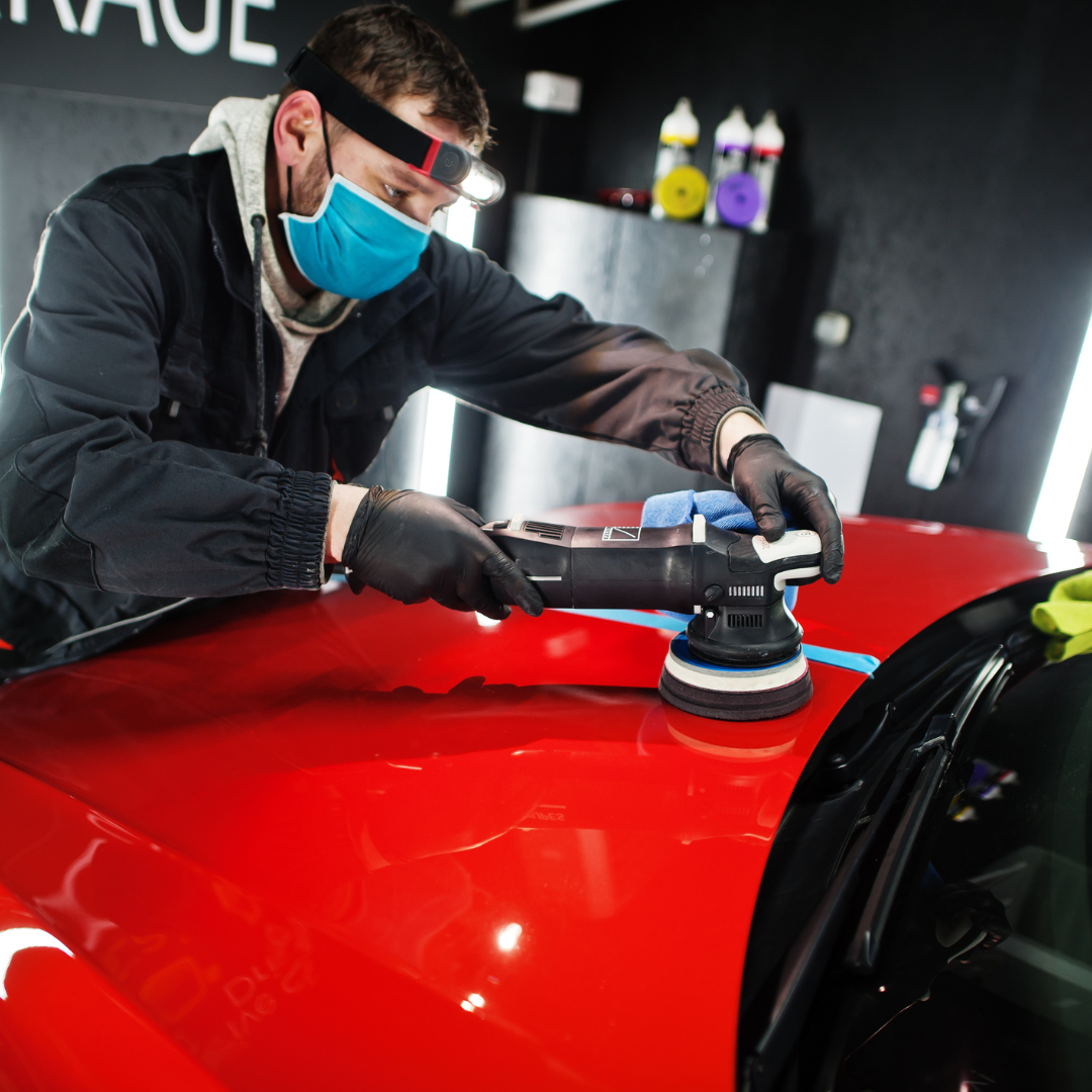 A man wearing a mask is polishing a red car